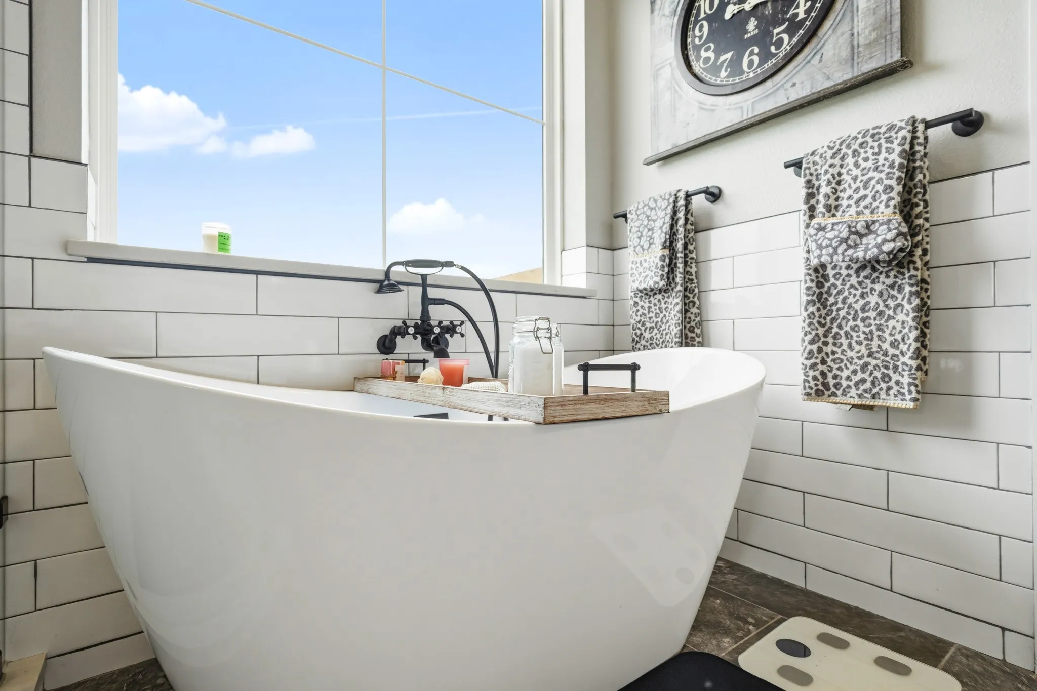 The bathroom features a white freestanding tub with a dark-toned faucet, white subway tile walls, and a window providing natural light