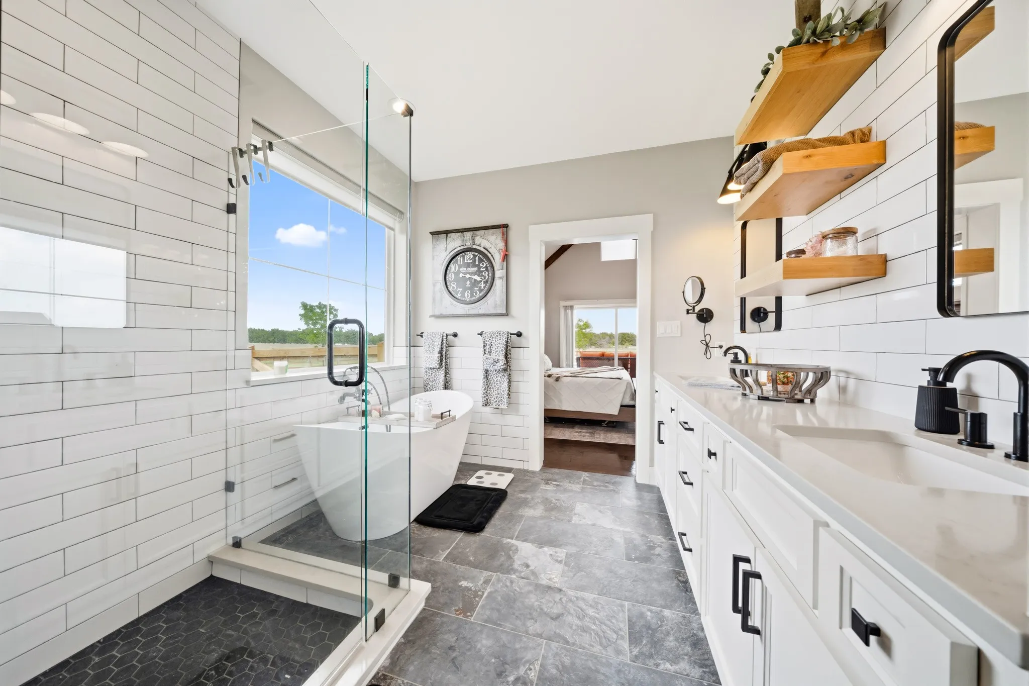 Well-appointed bathroom featuring a freestanding soaking tub, a spacious glass-enclosed shower with dark-tiled flooring, and a long vanity with dual sinks