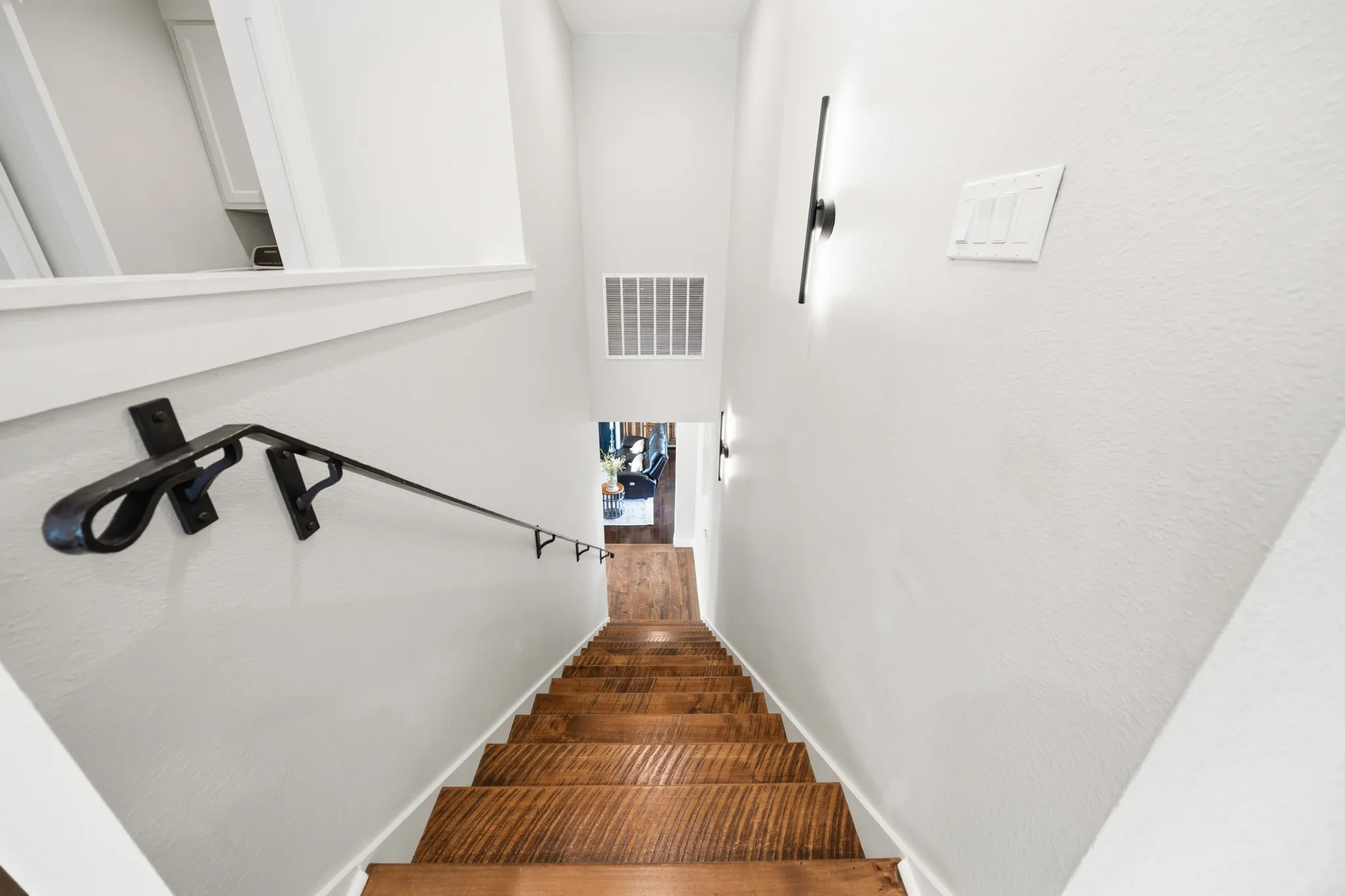 Staircase featuring rich wood treads, a dark-toned handrail, and modern wall sconces providing illumination