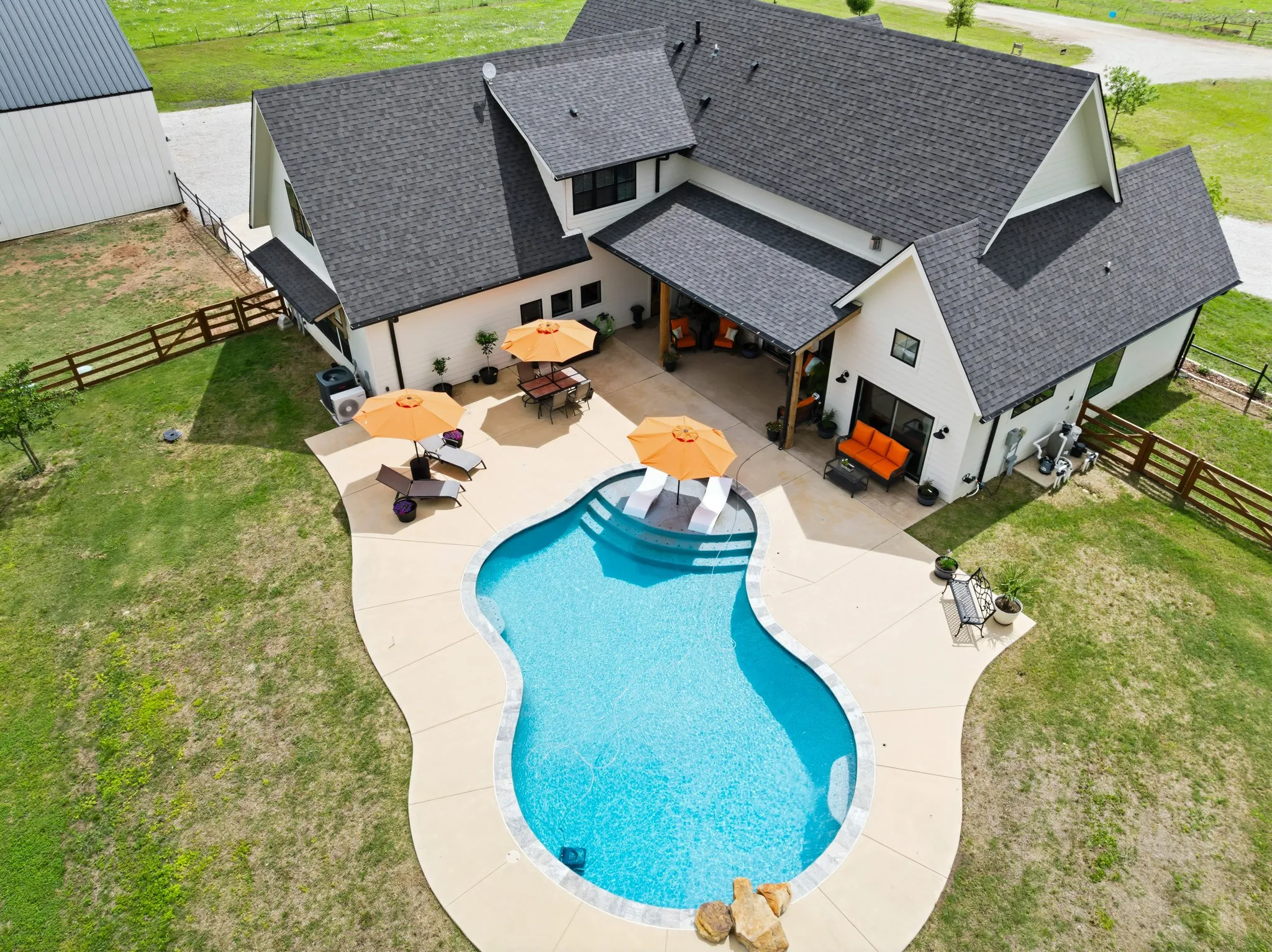 This property features a dark-shingled roof, white siding, and a large inground pool with a surrounding concrete patio