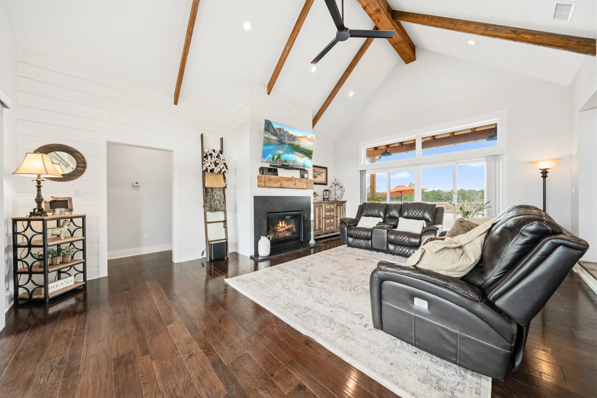 This living room features dark hardwood flooring, a vaulted ceiling with exposed wooden beams, and a fireplace