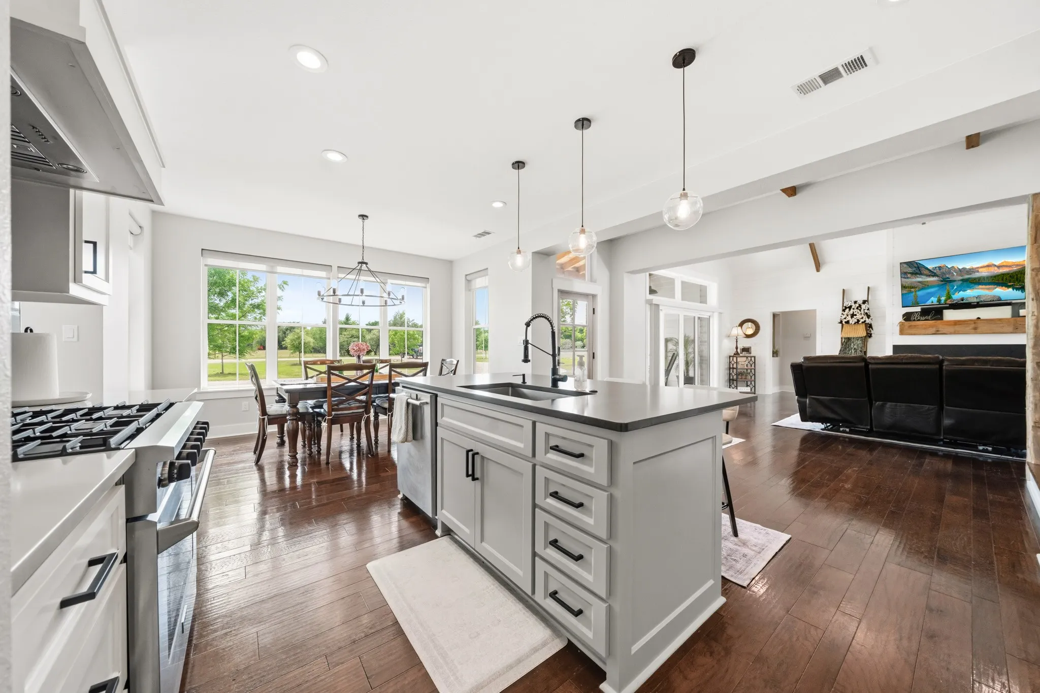 Open concept living space featuring rich hardwood flooring, a modern kitchen island with pendant lighting, and a dining area with a view of the outdoors