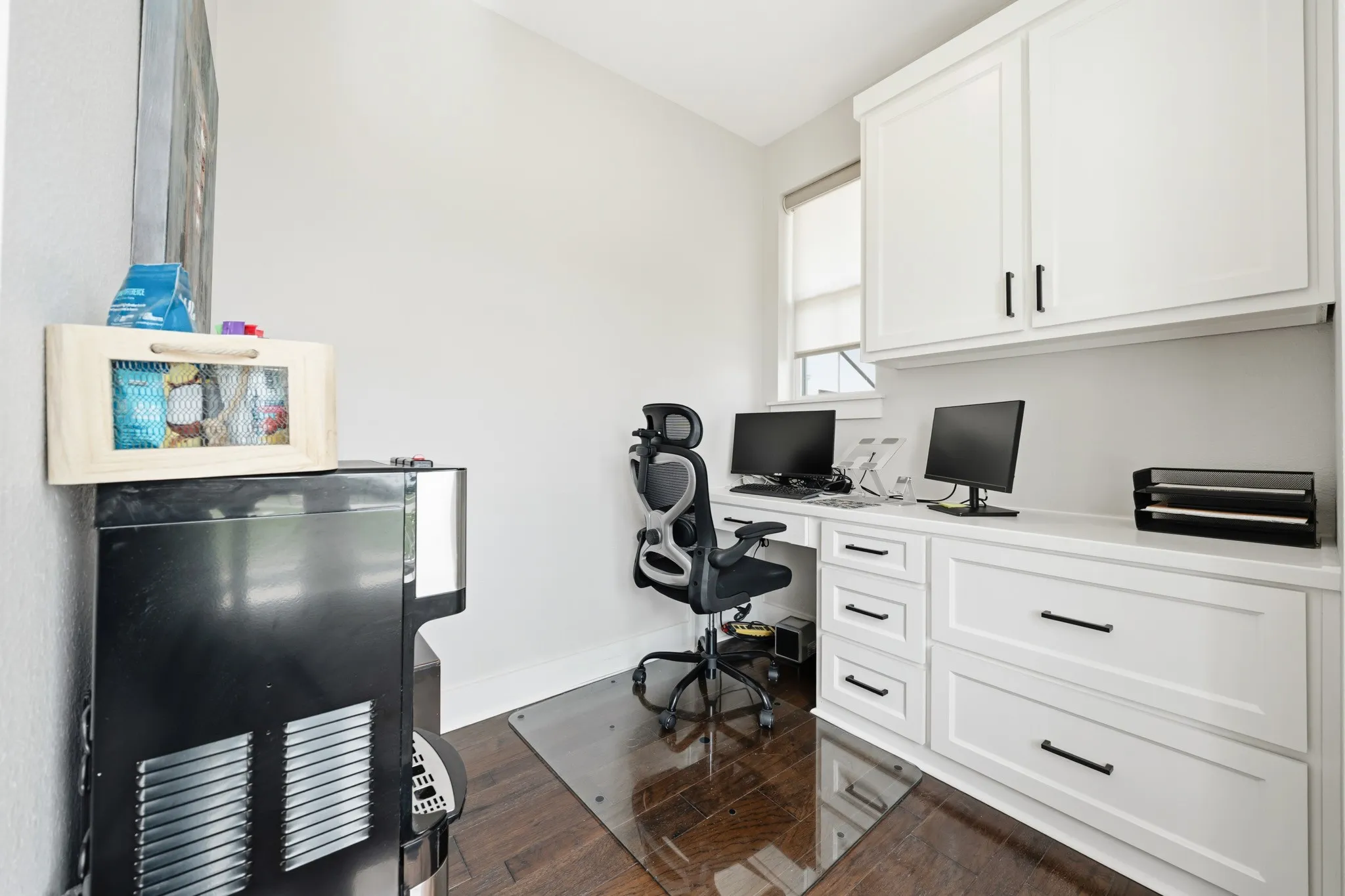 Dedicated office space featuring built-in white cabinetry with black hardware, a desk area with a window, and wood flooring