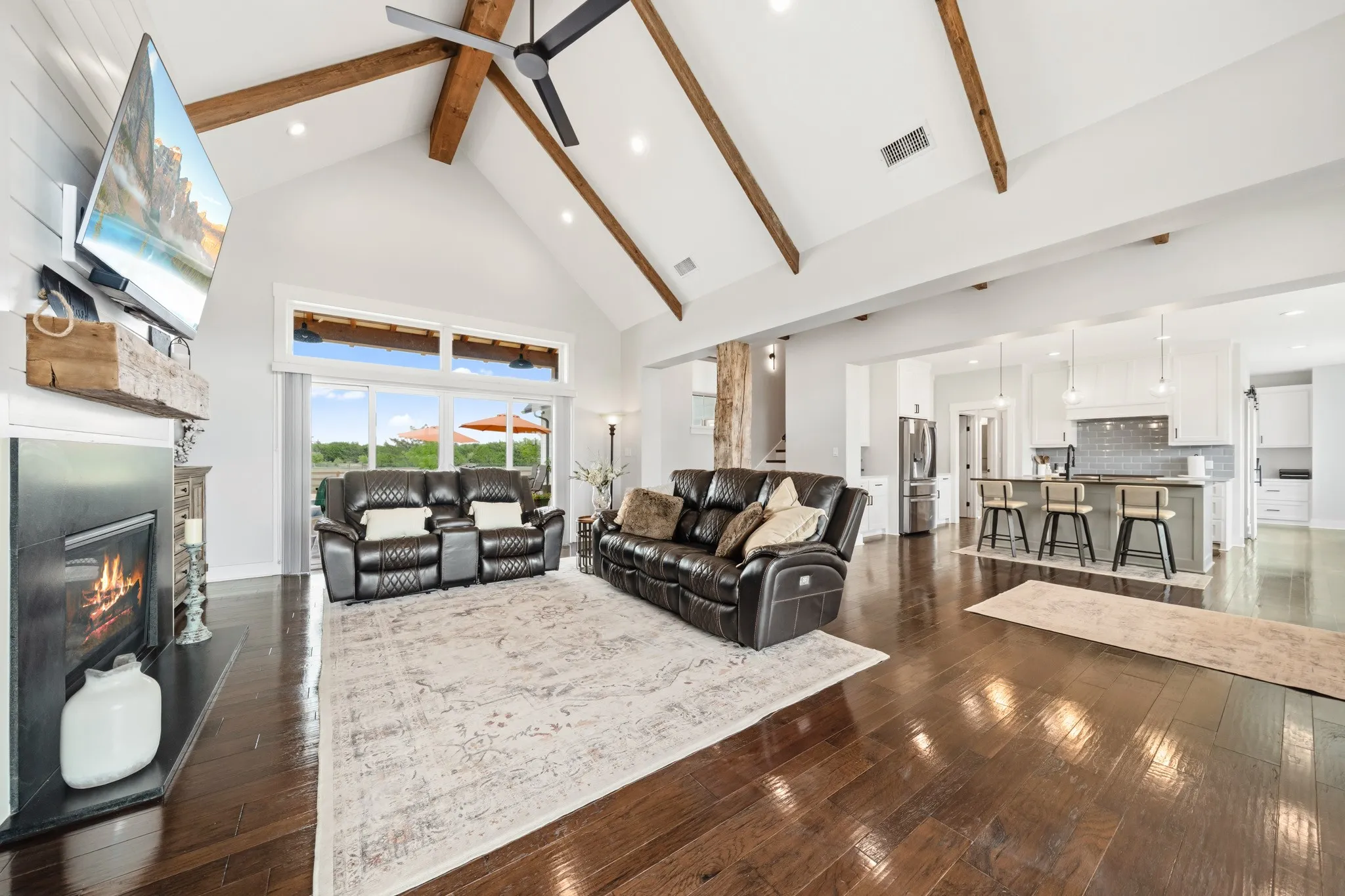 Expansive living area featuring vaulted ceilings with exposed wood beams, a fireplace, and hardwood floors