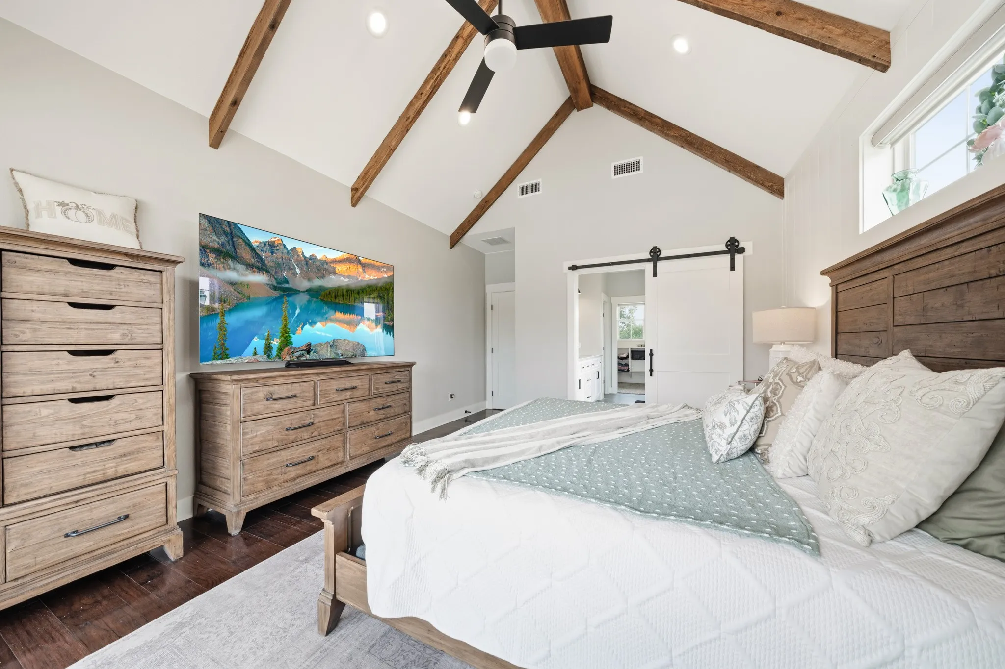 Bedroom featuring hardwood floors, a vaulted ceiling with exposed wooden beams, a ceiling fan, and a sliding barn door