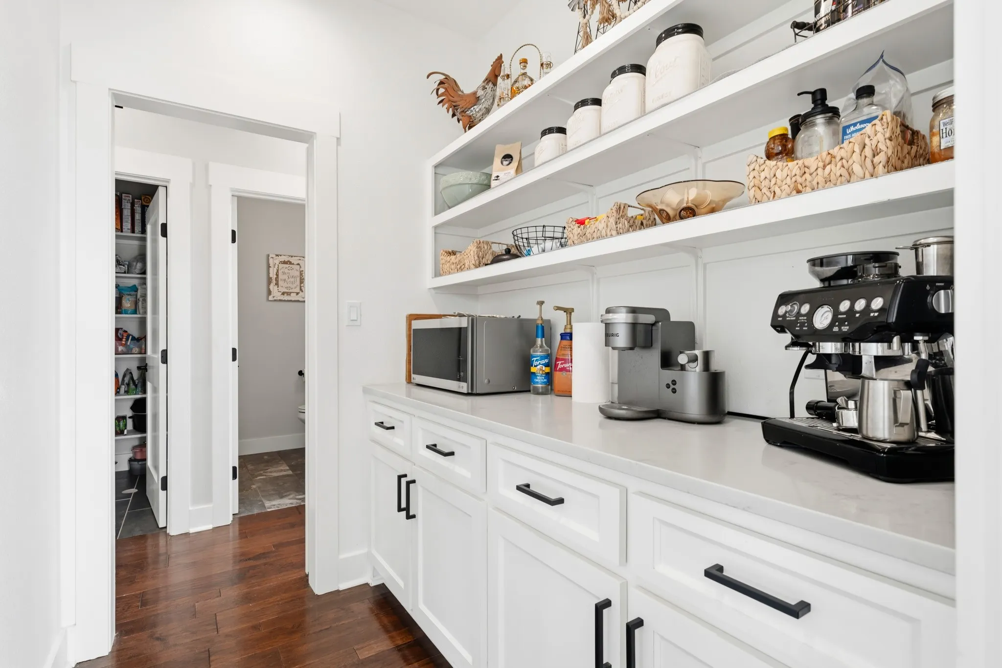 This space features white cabinetry with dark hardware, a light-colored countertop, and open shelving