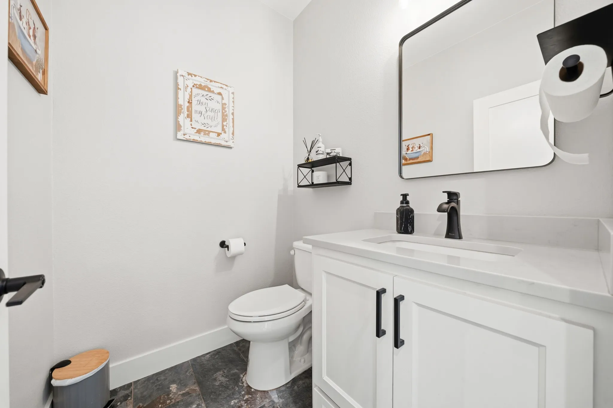 This well-appointed bathroom features a white vanity with a light-colored countertop, a black framed mirror, and a white toilet
