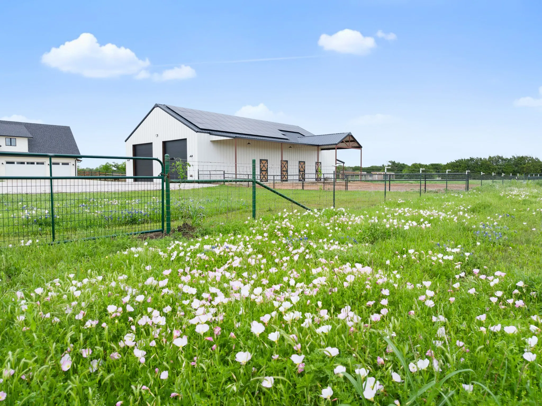 The property features a white barn with a dark roof and solar panels, a covered outdoor area, and fenced paddocks