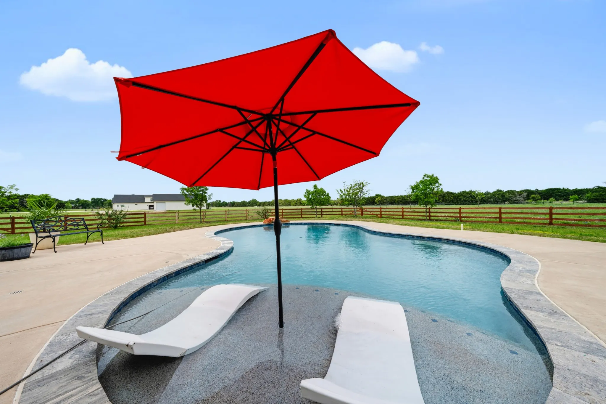 The property includes a shaped swimming pool with integrated sun loungers and a vibrant red umbrella