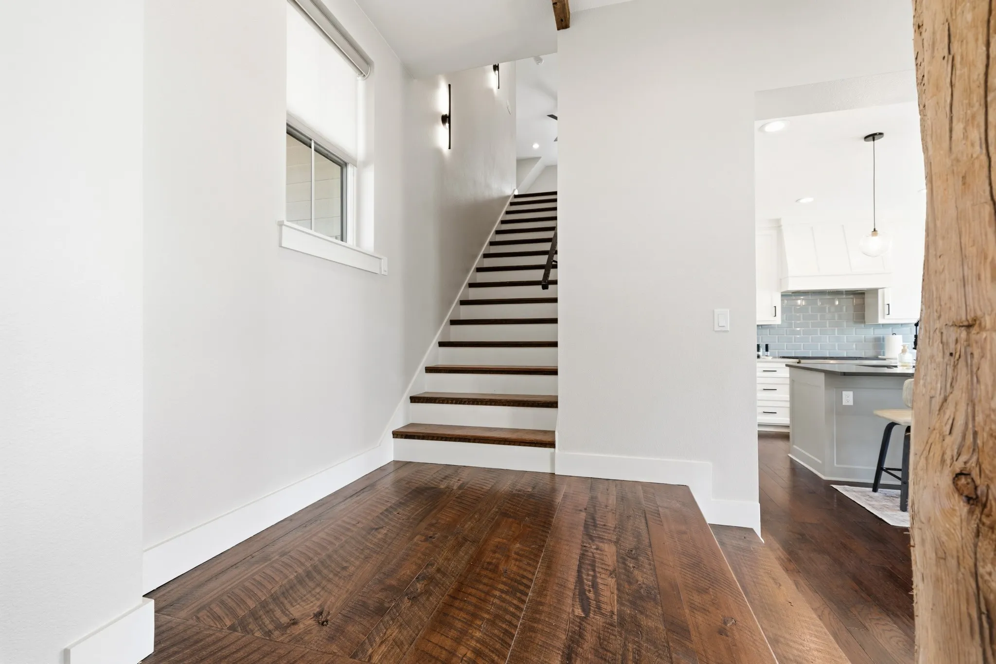 The property features rich hardwood flooring, a staircase with dark wood treads and risers, and a window with a roller shade
