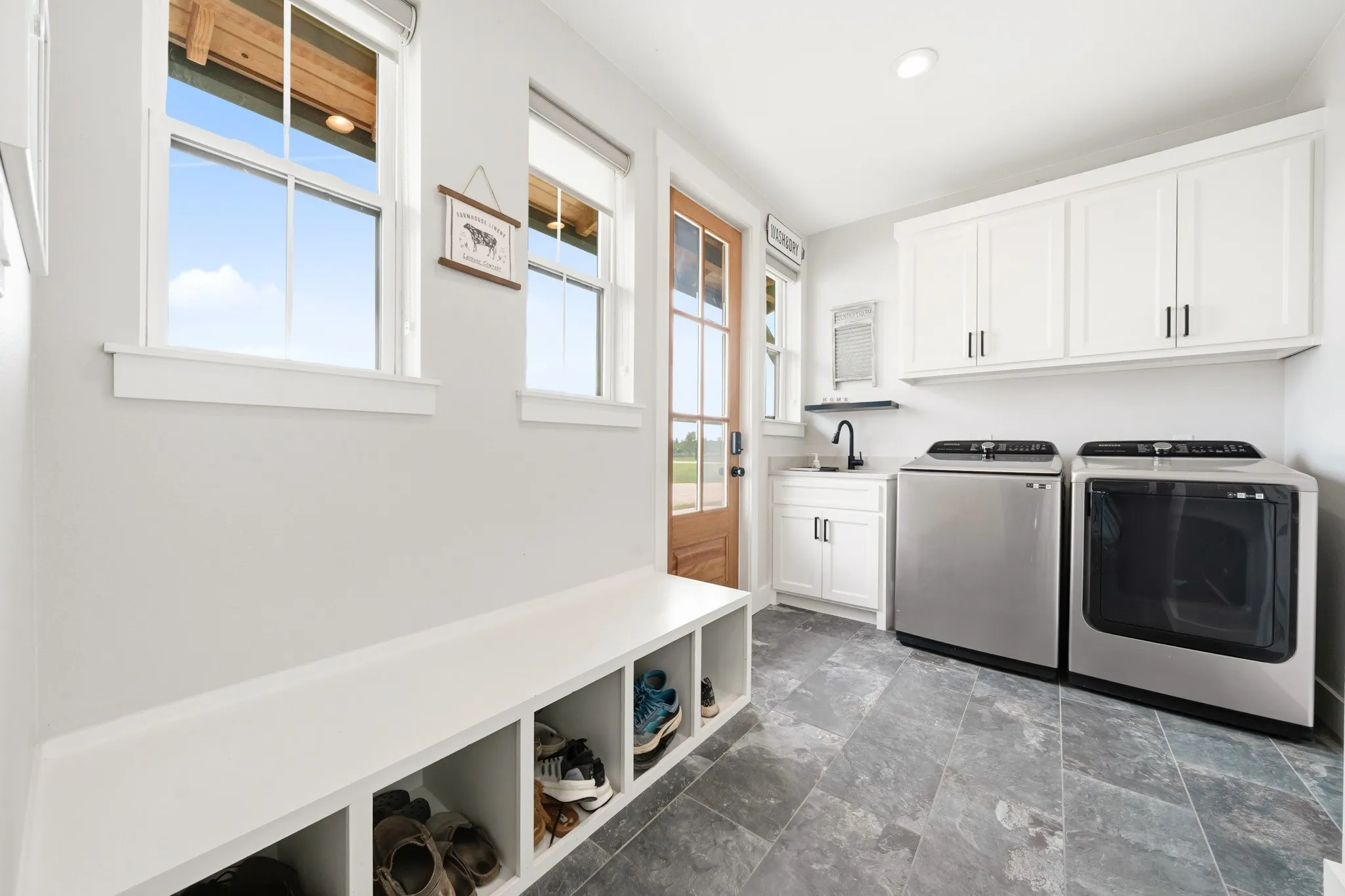 The utility room features a built-in white bench with storage cubbies, durable gray tile flooring, and white upper and lower cabinetry