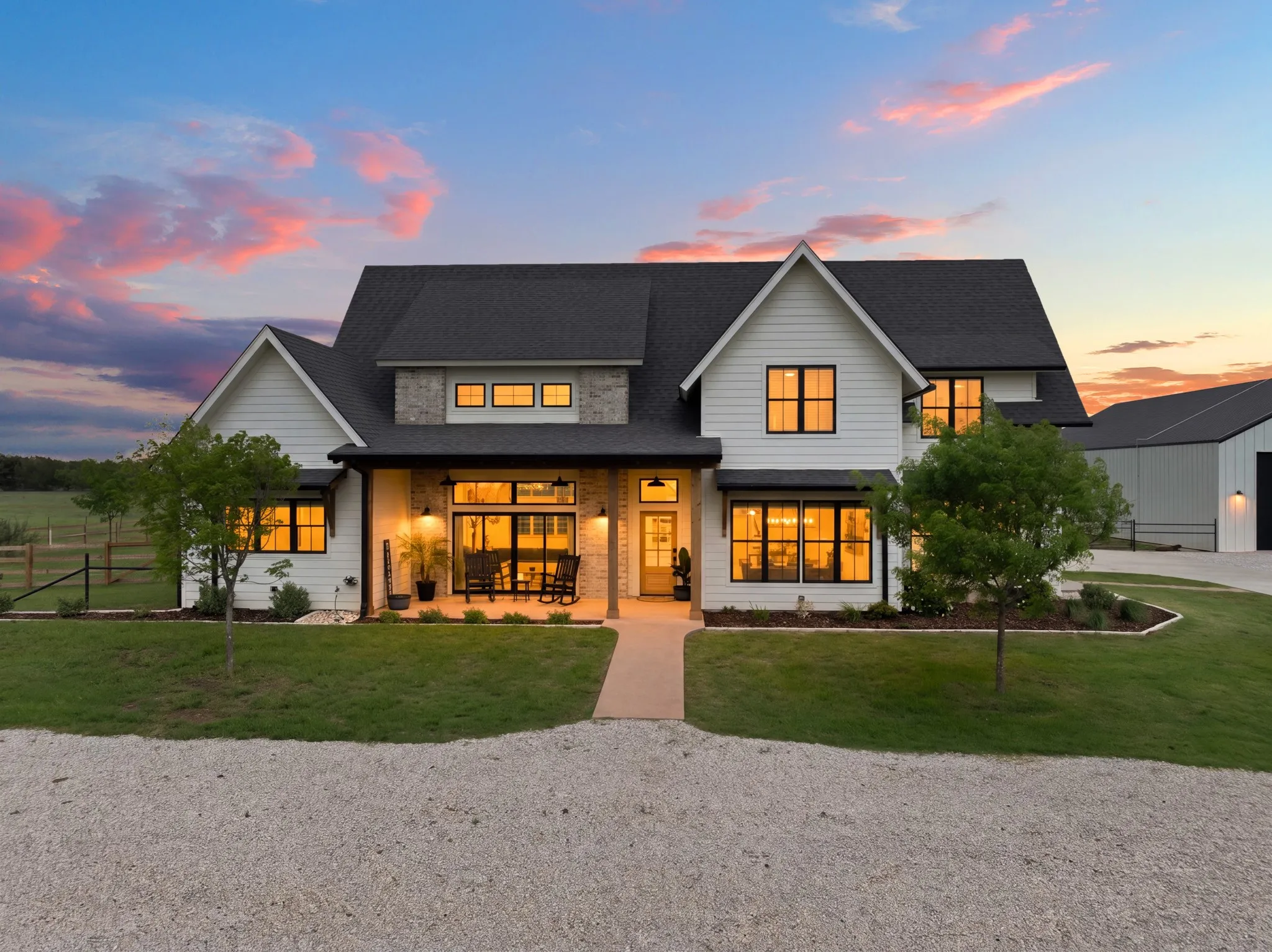 The property features a white exterior with dark-framed windows, a covered front porch, and a gravel driveway