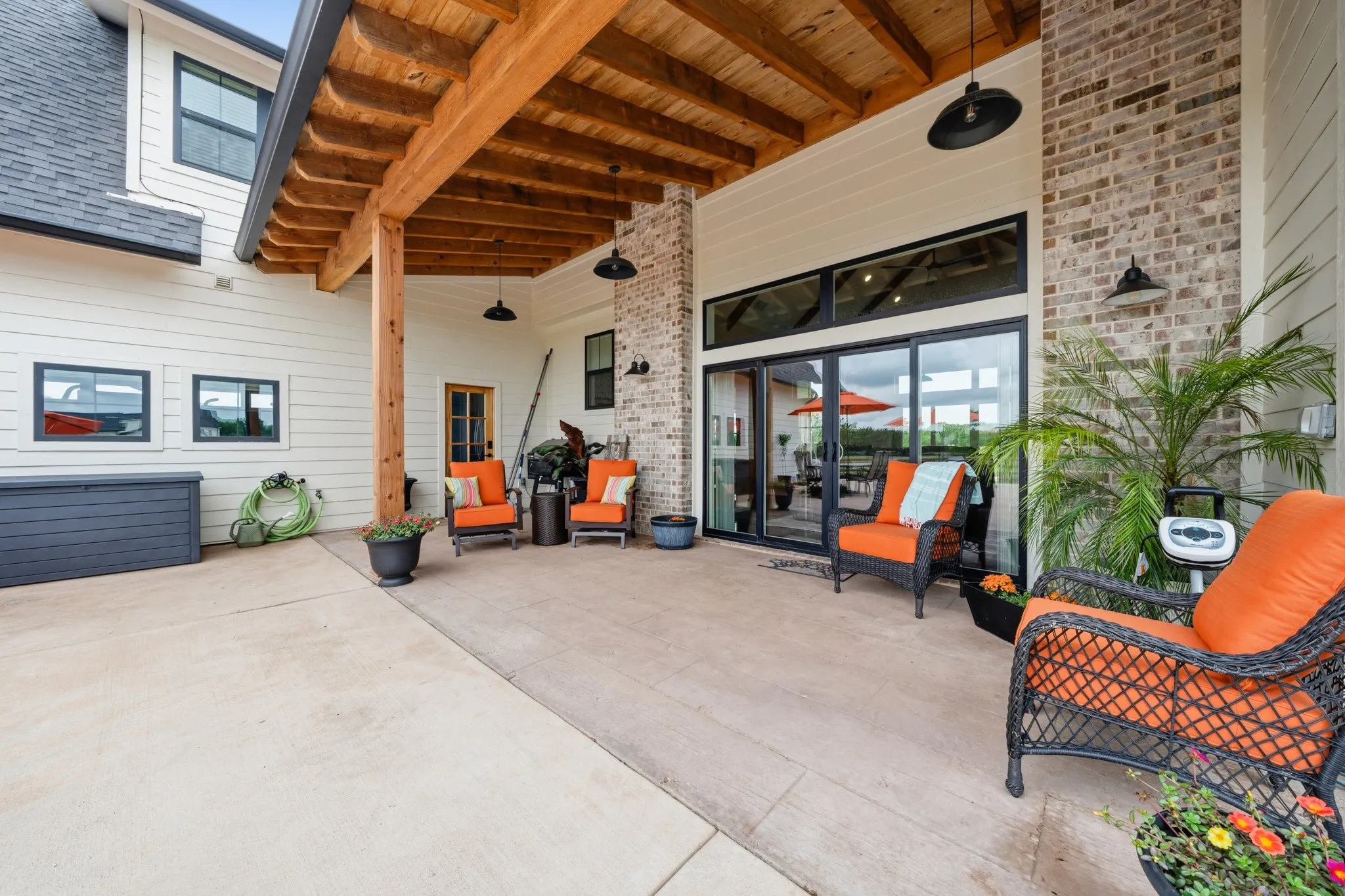 The property features an expansive covered patio with a wood-beamed ceiling, brick accents, and large glass sliding doors