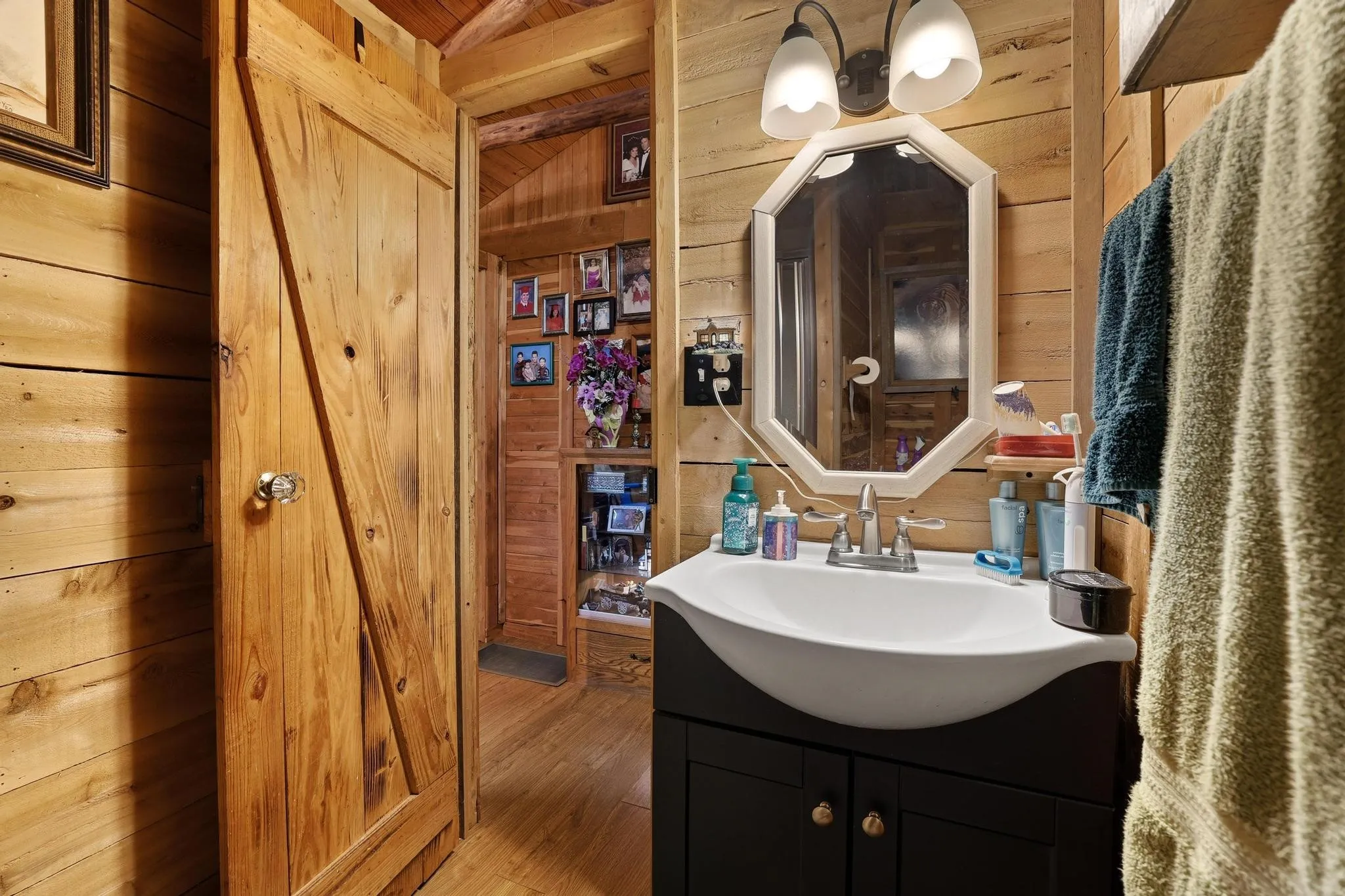 The bathroom features wood paneling, a vanity with a white basin sink, an octagonal mirror, and a wall-mounted light fixture