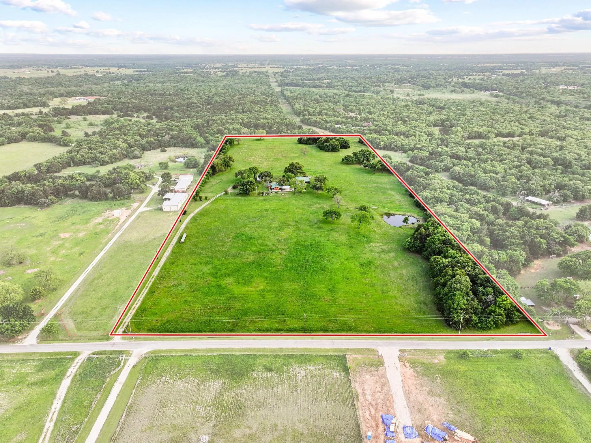 Expansive property offering extensive green acreage with trees, a pond, and road frontage