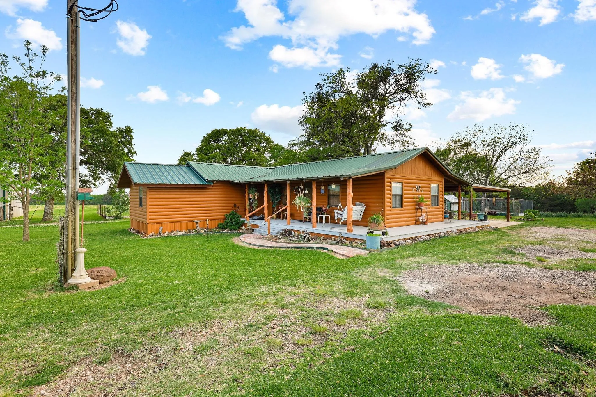 The property features a log cabin style exterior with a green metal roof, a wrap-around porch, and a spacious grassy yard