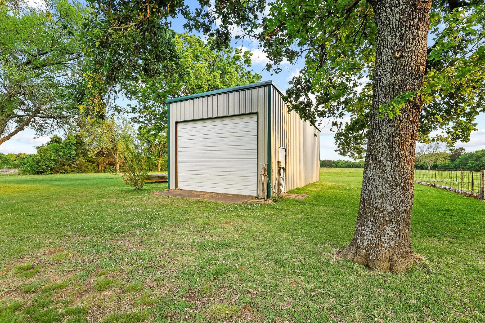 The property includes a detached metal building with a roll-up garage door and a side entry door, situated on a grassy area with mature trees