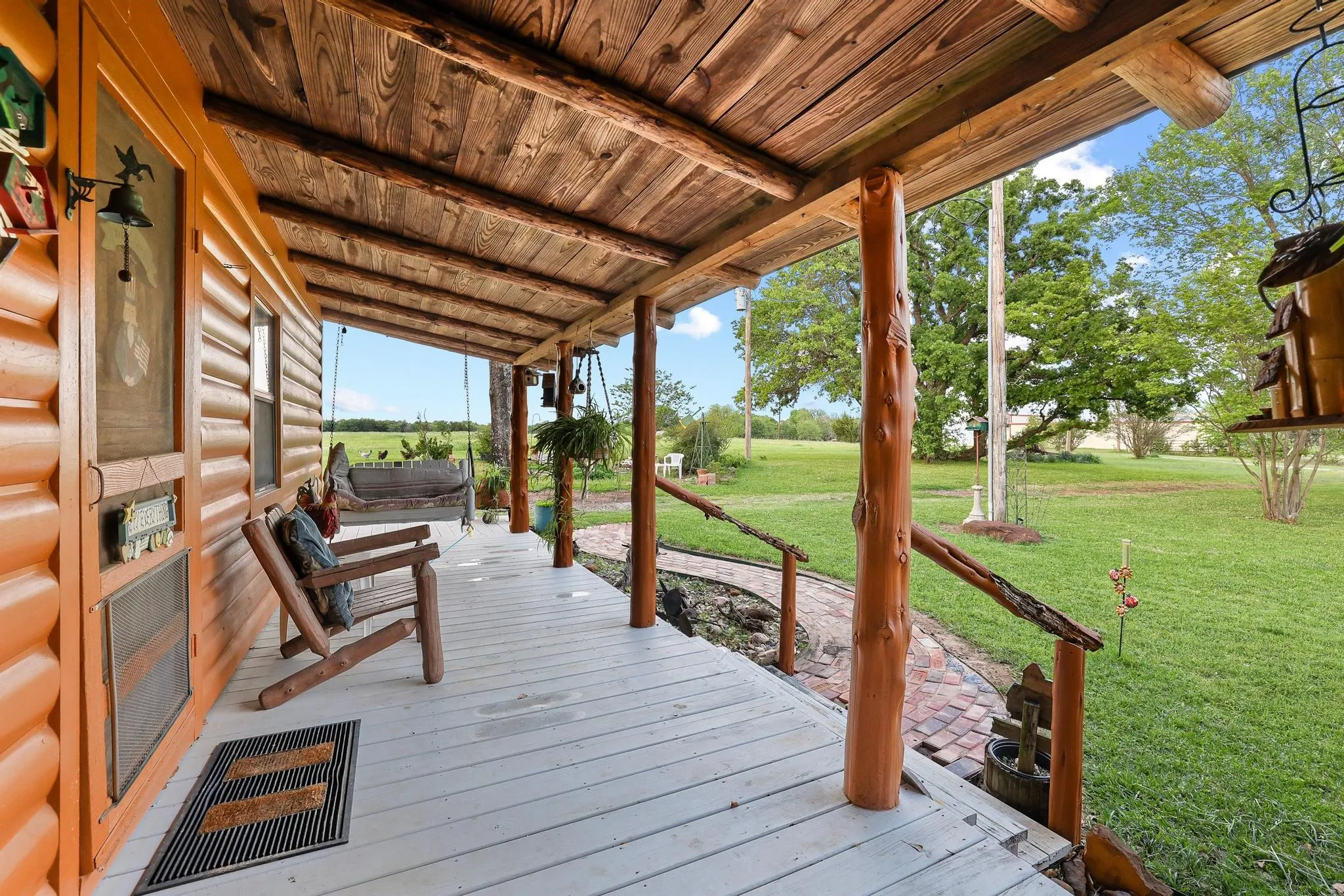 The property features a spacious covered porch with exposed wood beams and posts, offering views of the expansive green lawn and distant trees