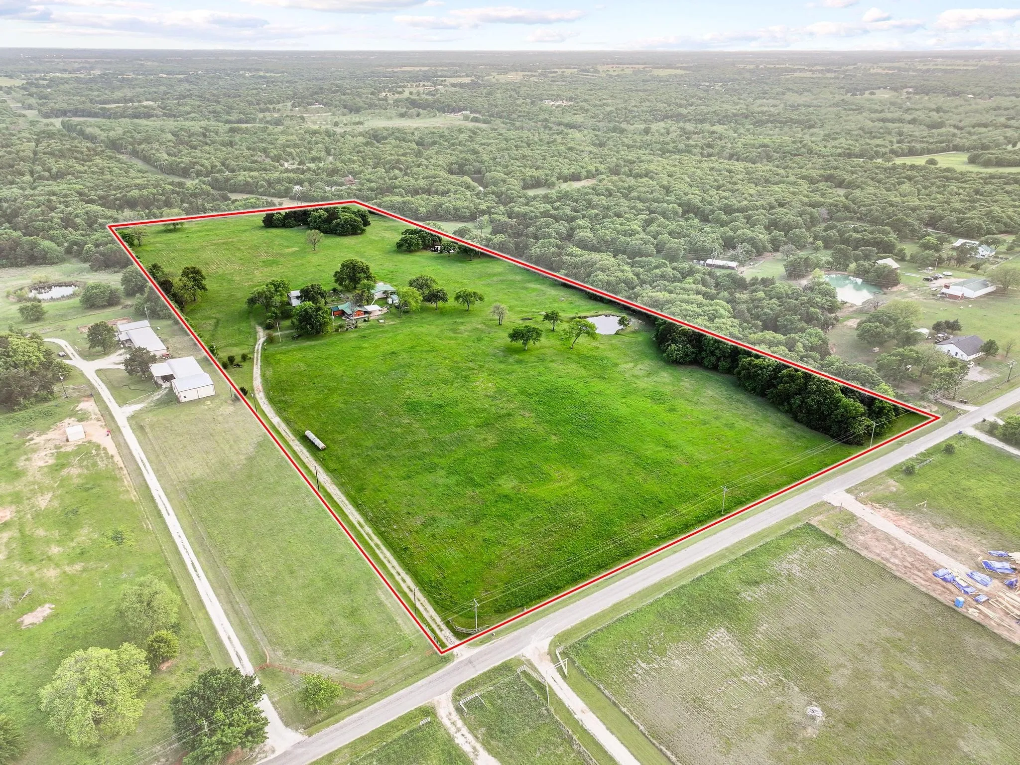 This property features expansive green fields with mature trees and a pond, bordered by a road