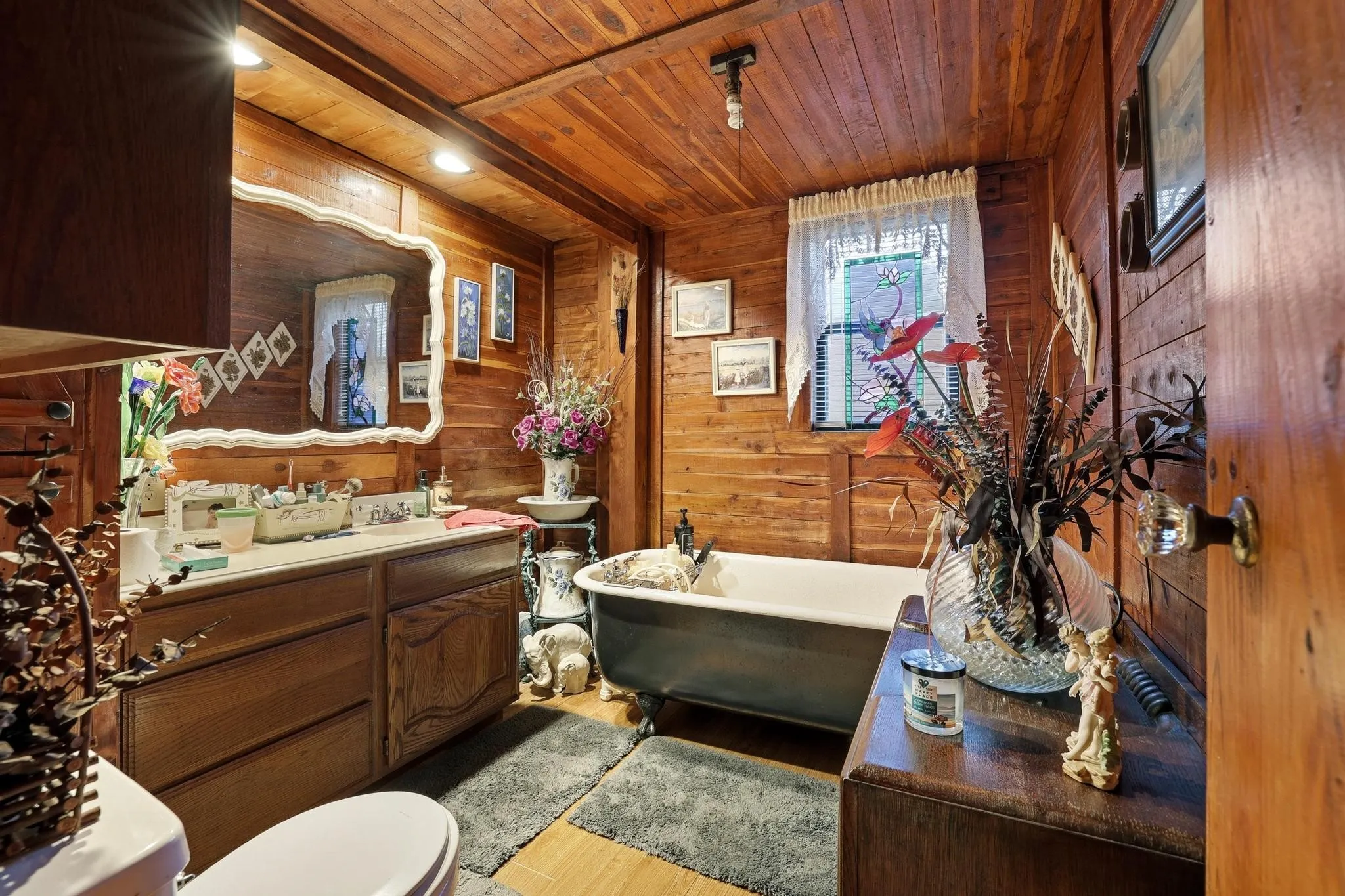 The bathroom features wood paneled walls, a single vanity with a white countertop, and a classic freestanding bathtub