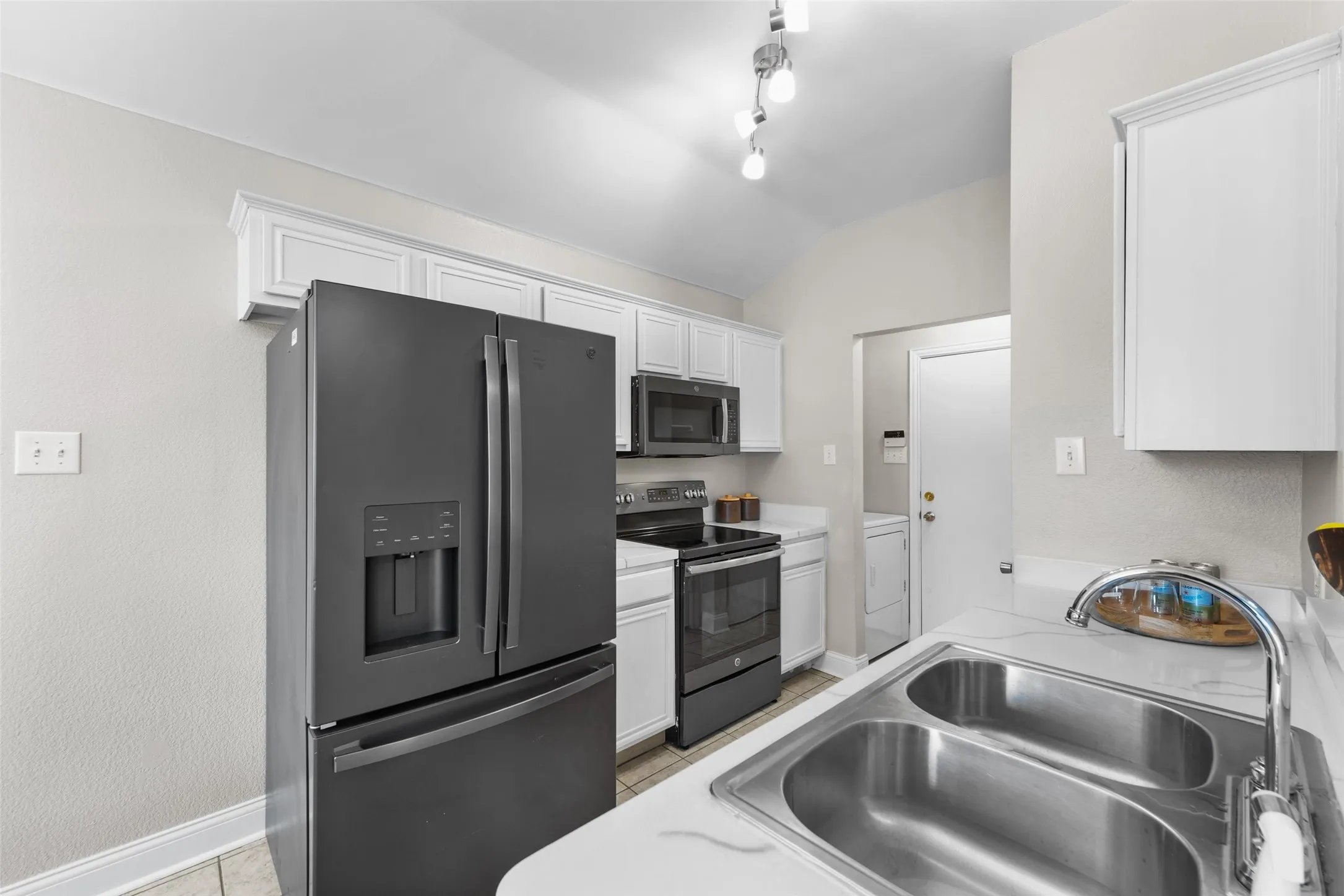 Kitchen with stainless steel appliances, white cabinets, light countertops, and light tile patterned flooring