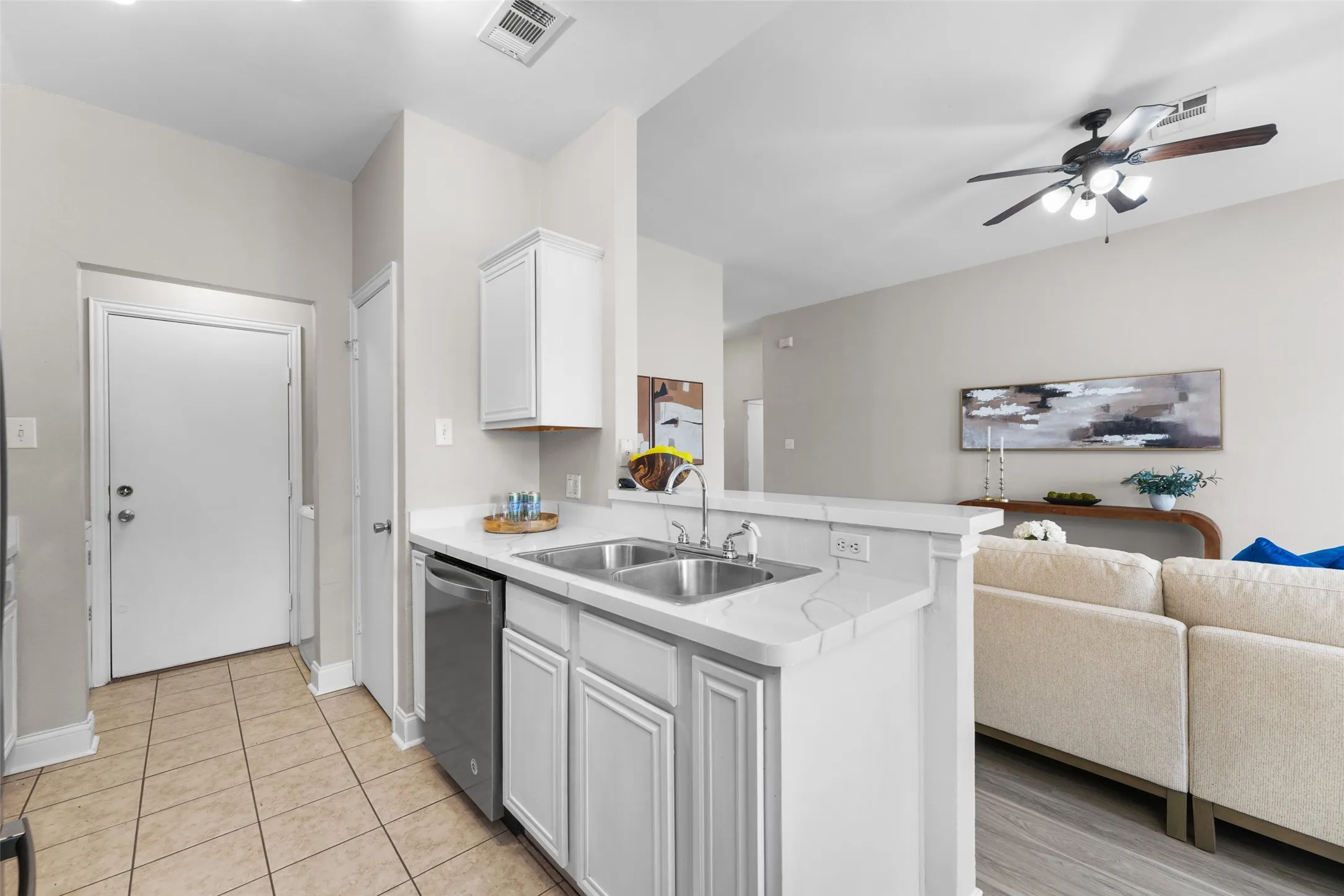 Kitchen featuring open floor plan, light countertops, white cabinets, stainless steel dishwasher, and ceiling fan