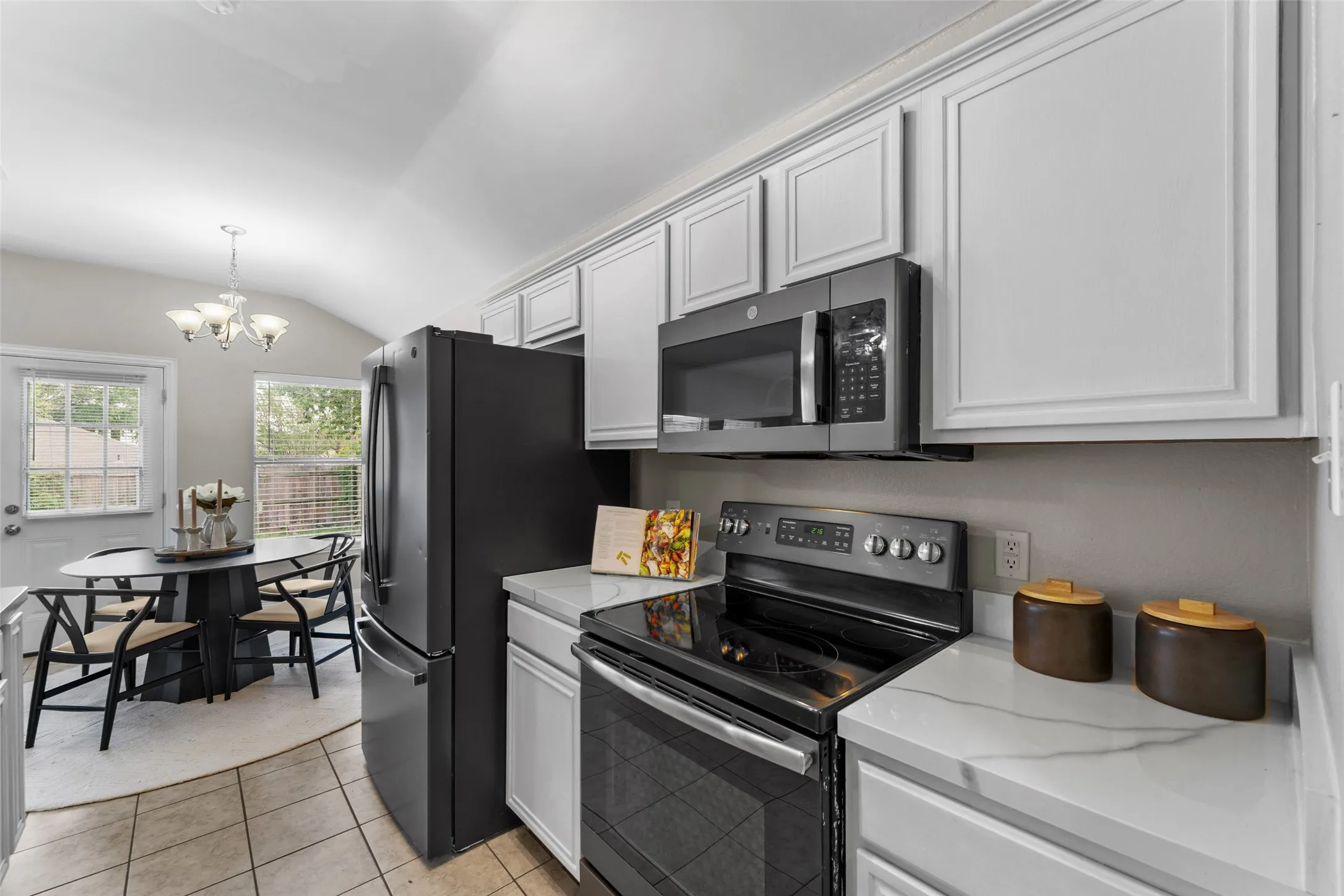 Kitchen featuring stainless steel appliances, lofted ceiling, suspended lighting, light tile patterned flooring, and light stone counters