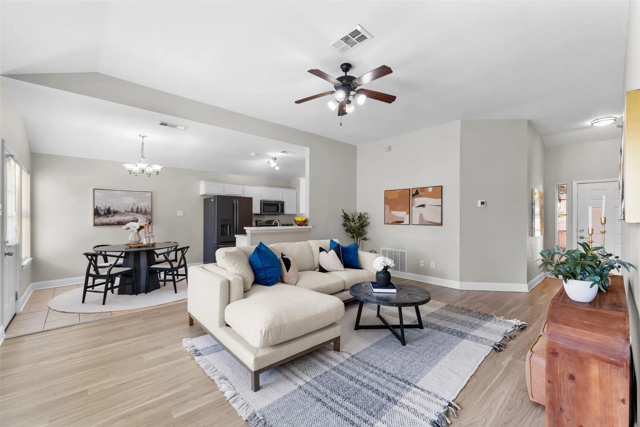 Virtually staged. Living area with light wood finished floors, ceiling fan, a chandelier, and lofted ceiling