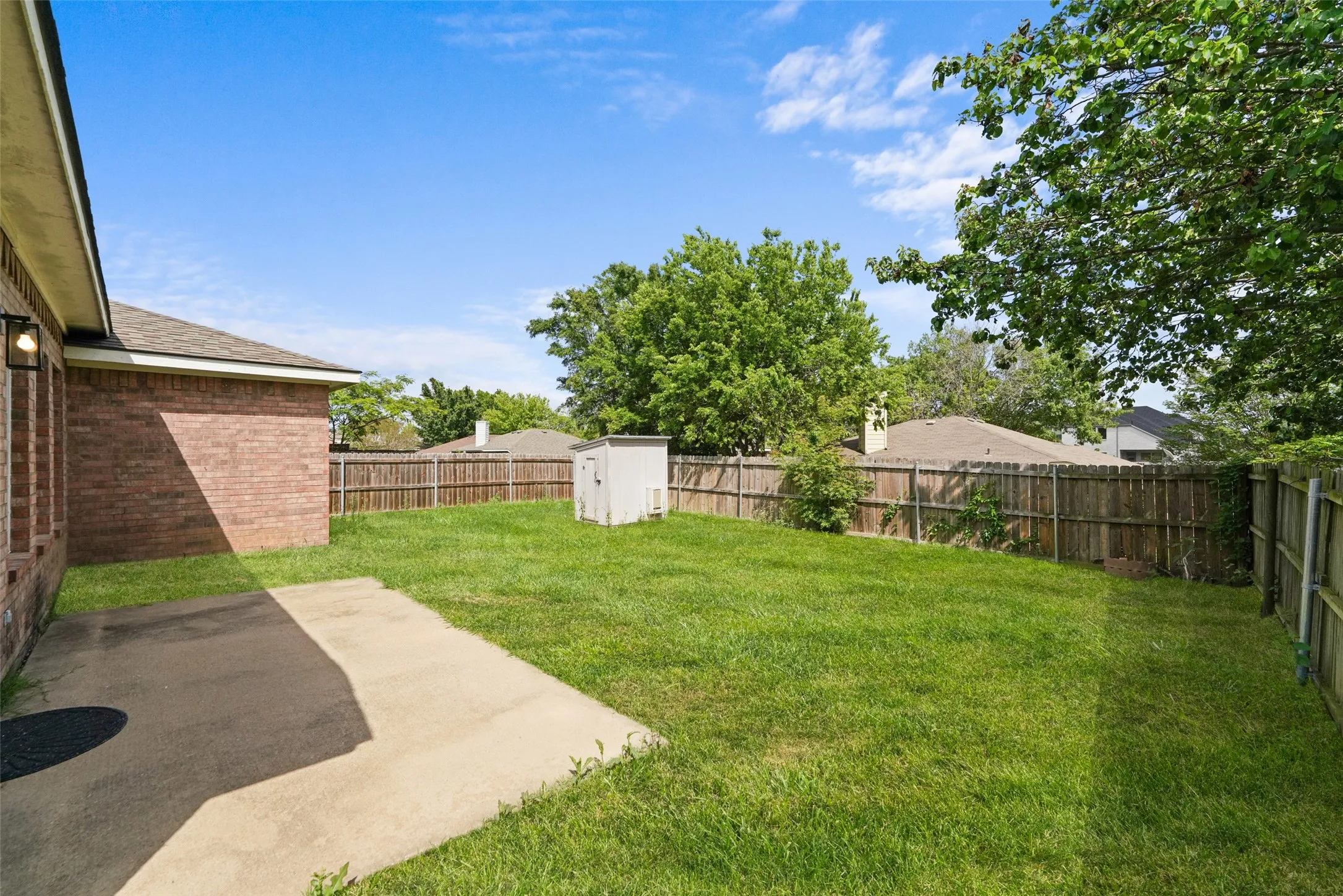 Fenced backyard featuring a storage shed and a patio area