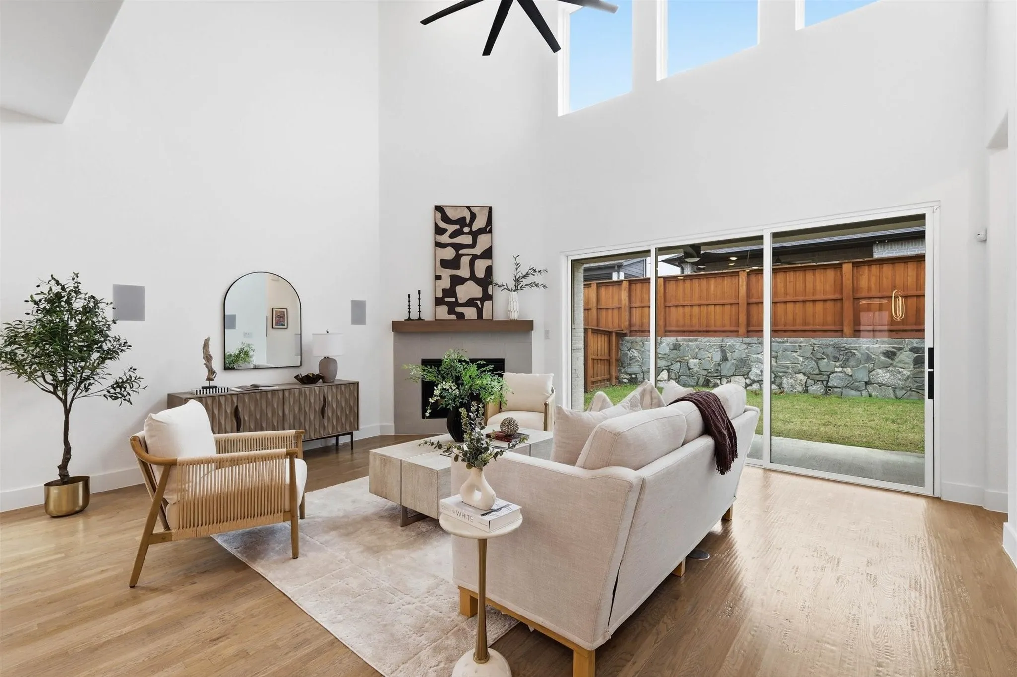 This living area features soaring ceilings, light-toned hardwood flooring, and large windows that provide abundant natural light