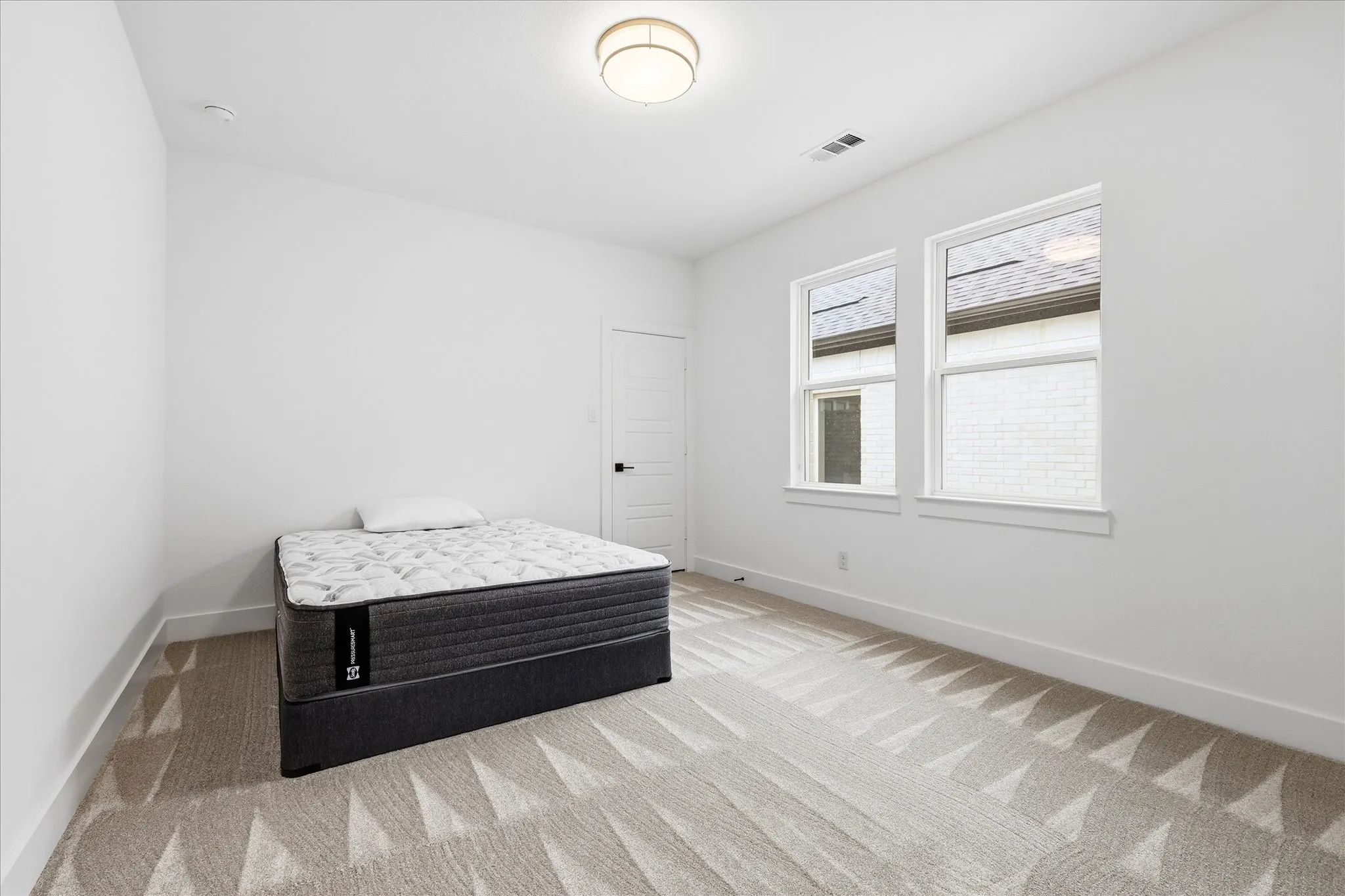 This room features two windows providing natural light, a neutral color palette throughout, and a textured carpet with a geometric pattern