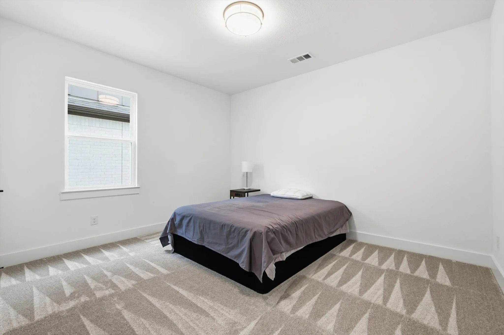 This room features a window providing natural light, white walls, and patterned carpeting