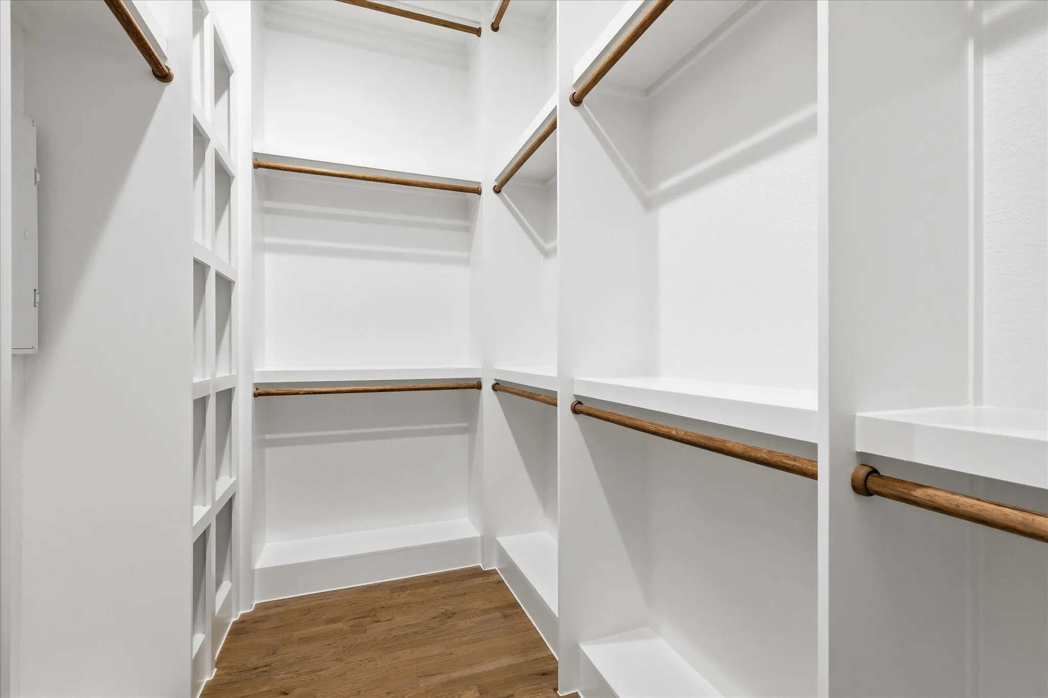 Spacious closet featuring white built-in shelving, hanging rods, and wood flooring