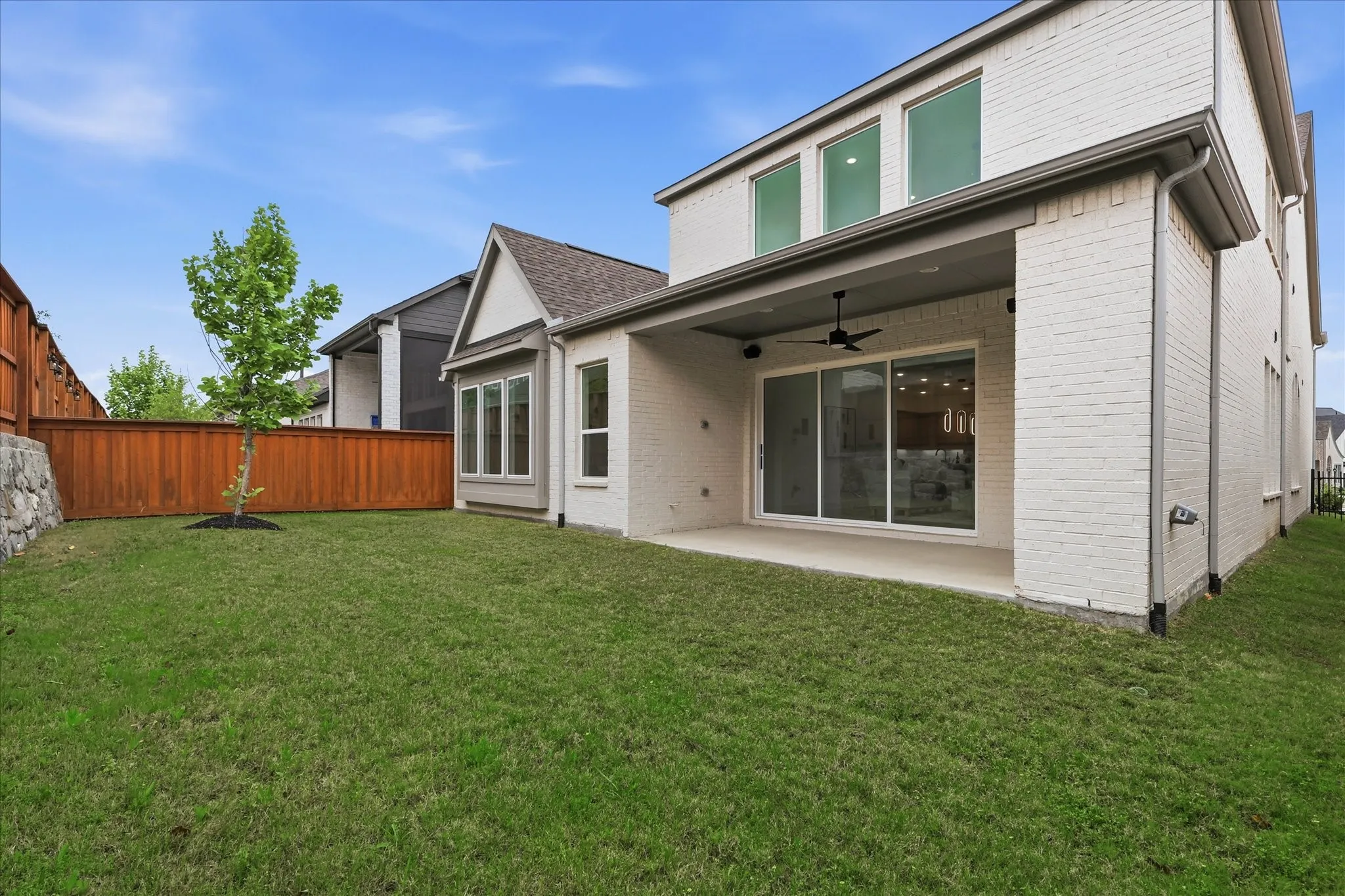 The property features a spacious lawn, a covered patio with a ceiling fan, and sliding glass doors