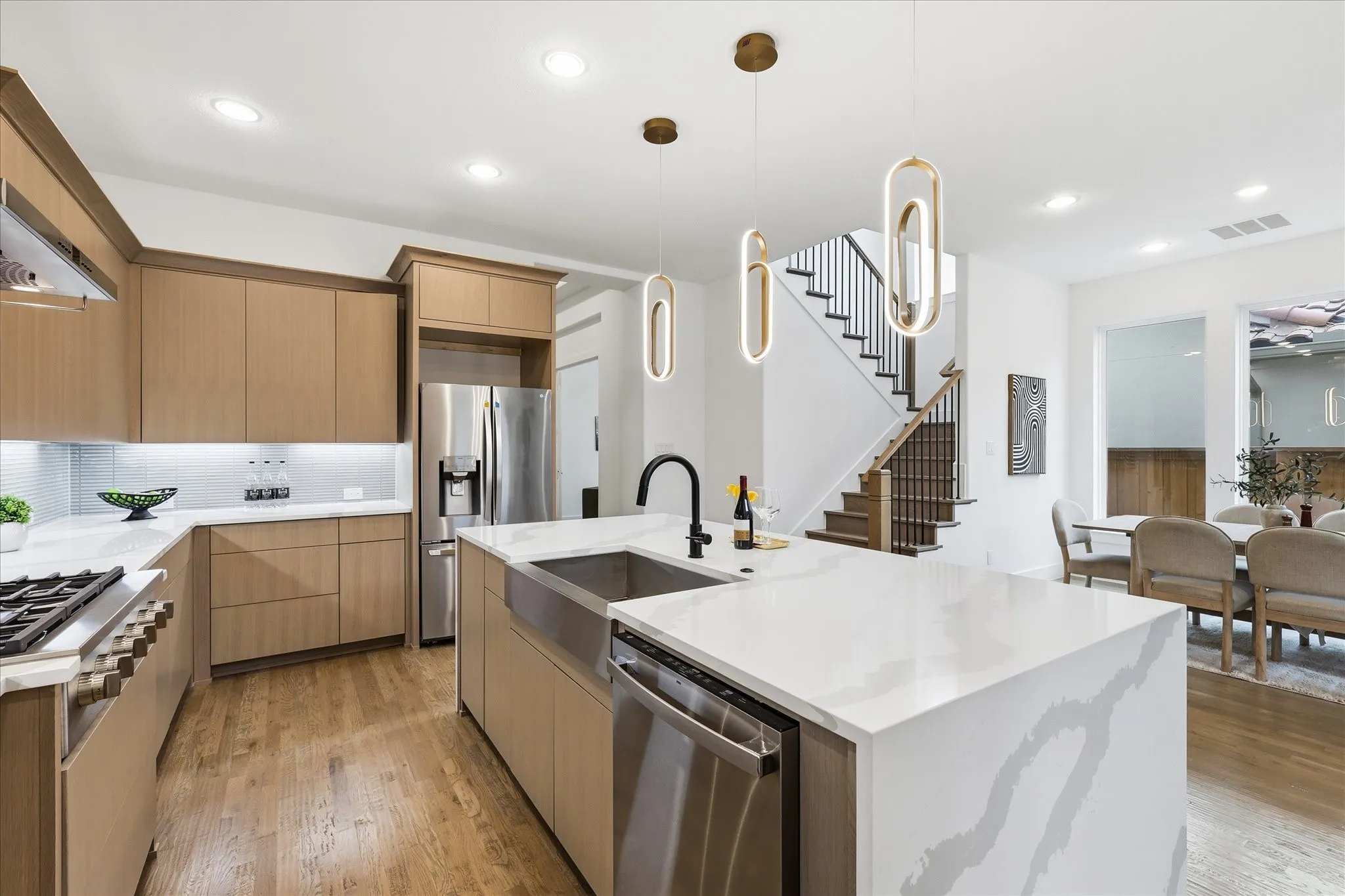 Contemporary kitchen featuring light wood cabinetry, stainless steel appliances, a large island with a sink, and hardwood flooring
