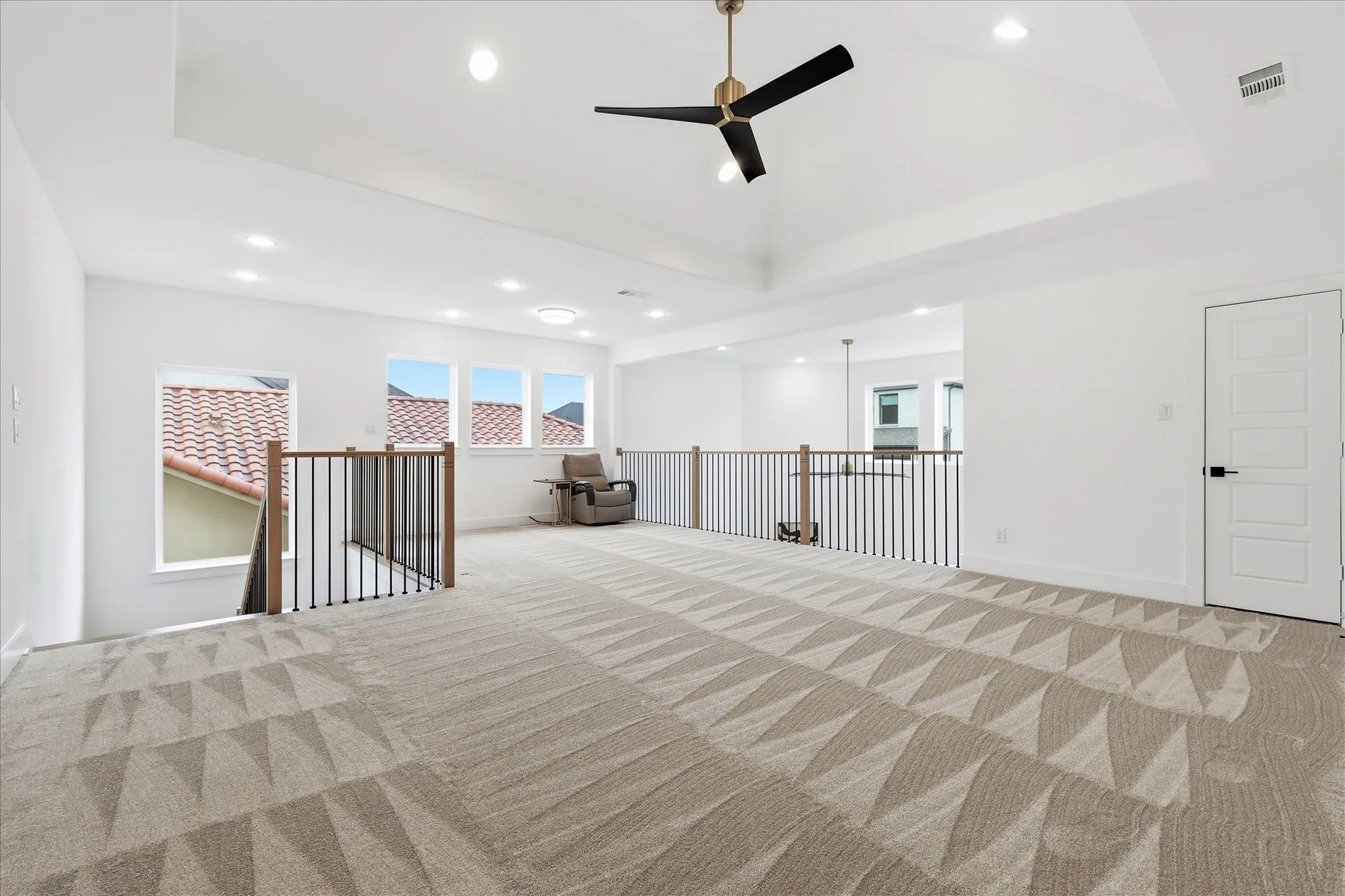 Spacious loft area featuring patterned carpet, a ceiling fan, and large windows providing natural light