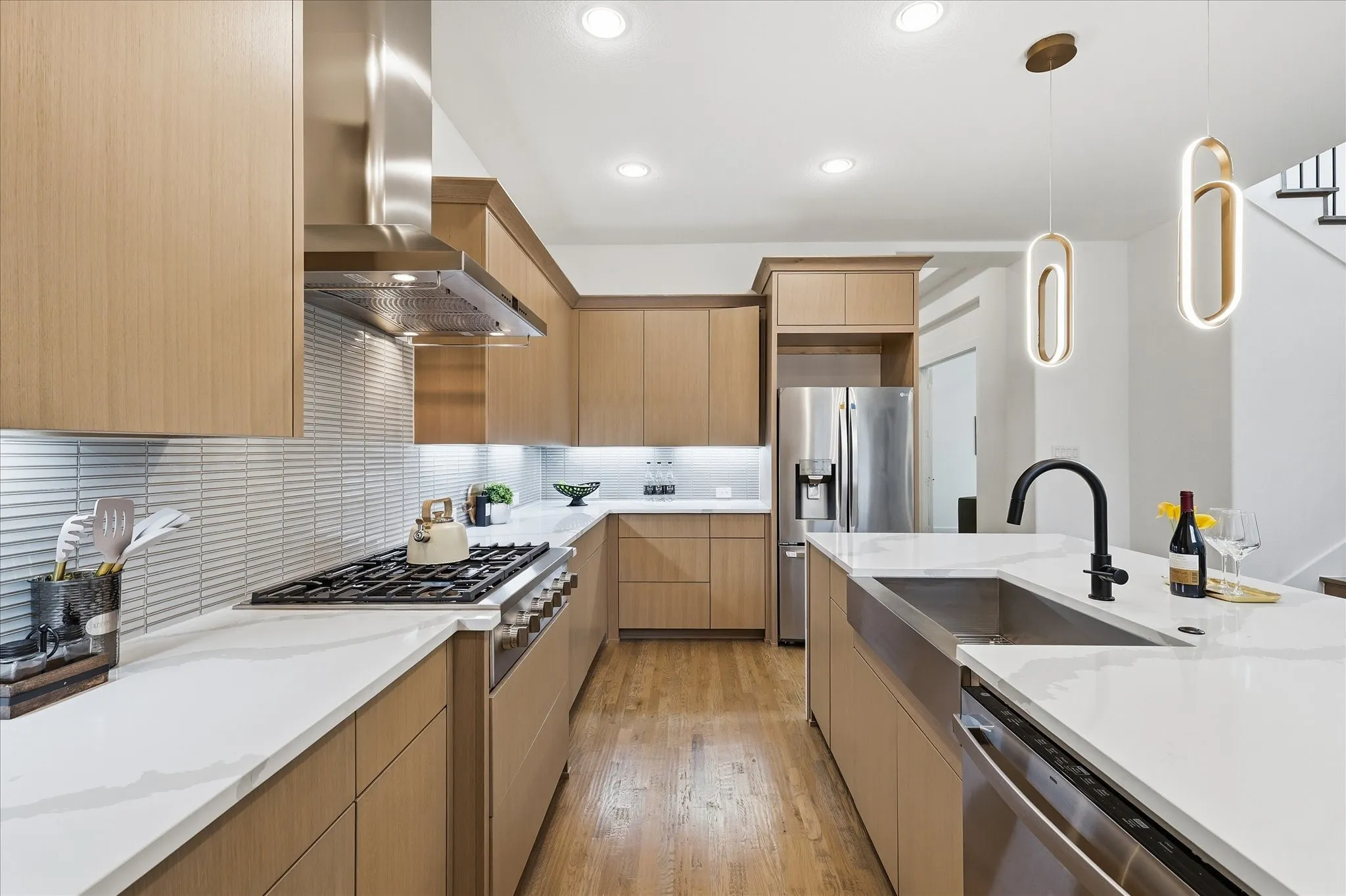 Contemporary kitchen featuring light wood cabinetry, white countertops, stainless steel appliances, and hardwood floors