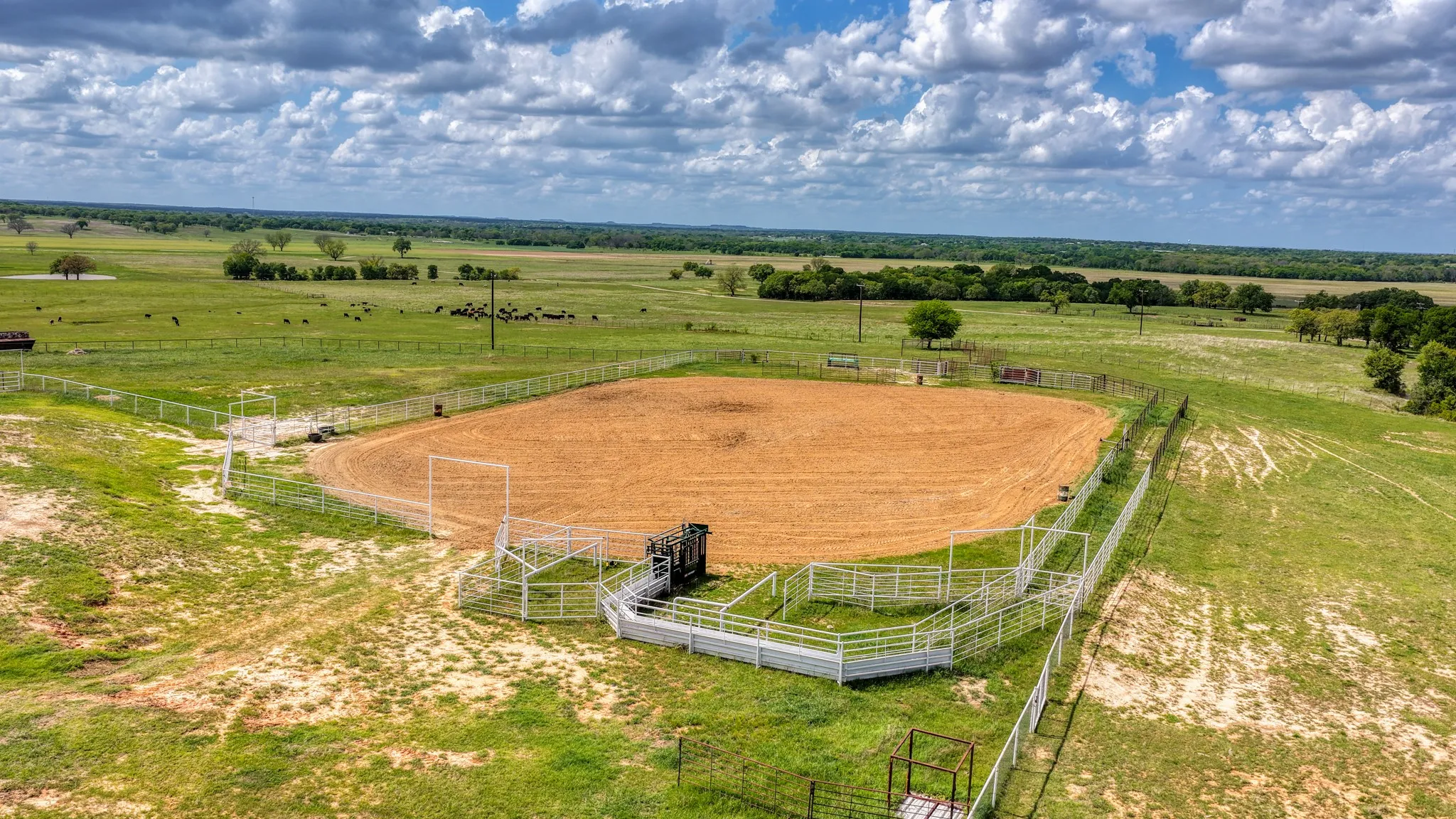 Expansive aerial view of the property, showcasing a well-maintained arena with metal fencing and chutes