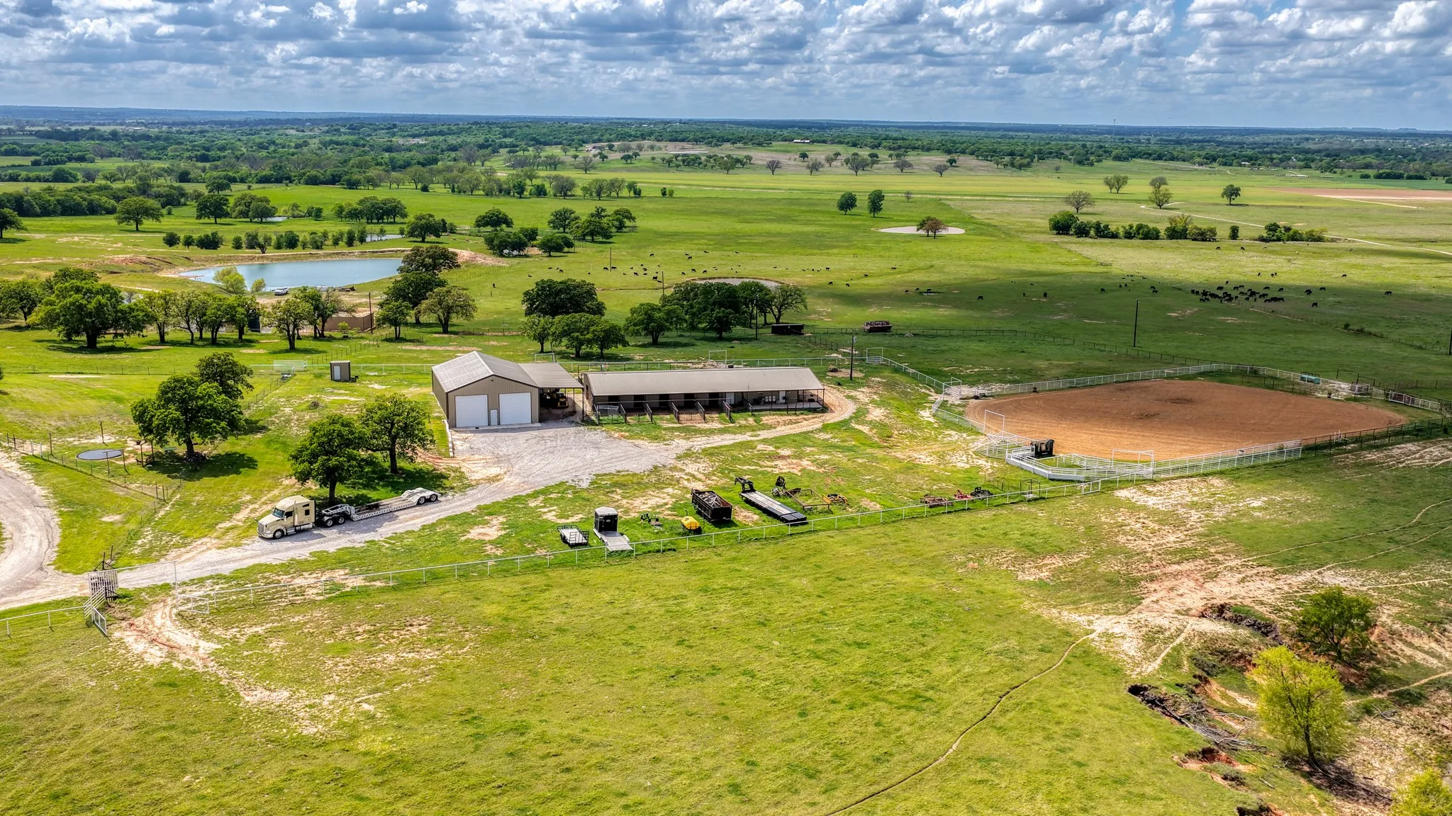 This property features a barn, a horse riding arena, and an open pasture with a pond, all surrounded by mature trees