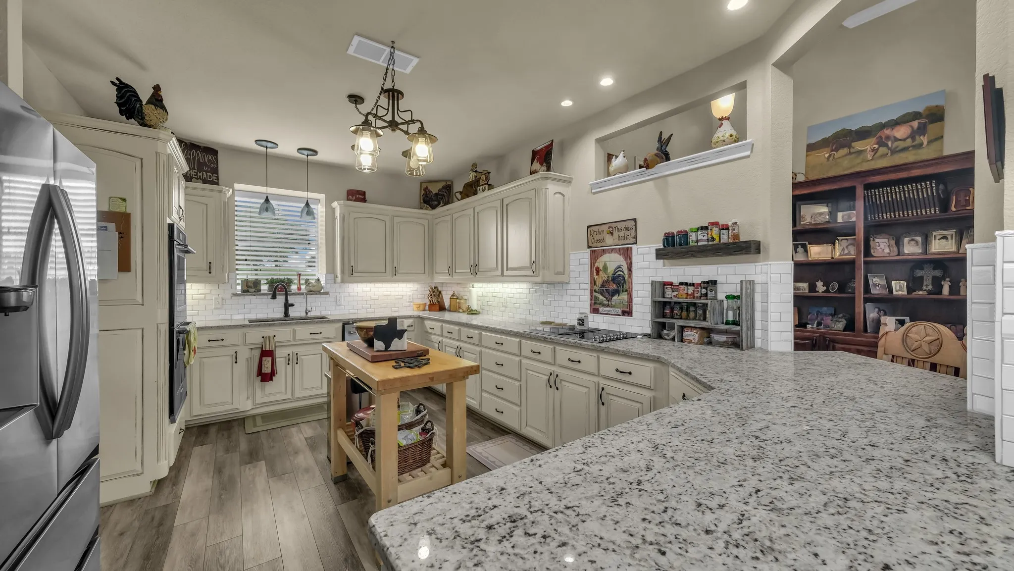 The kitchen features extensive cream-colored cabinetry, a white subway tile backsplash, and light-colored granite countertops