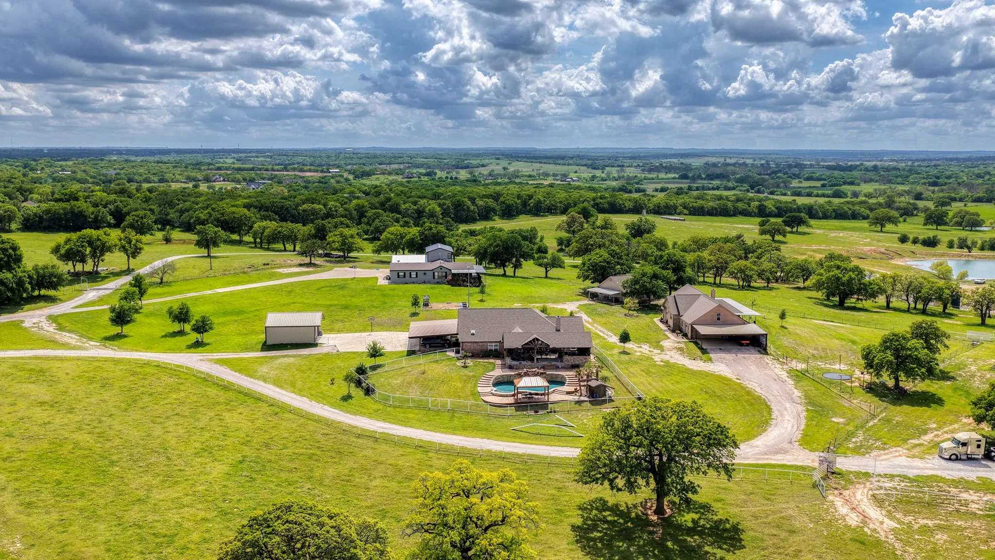 The property features a main residence with an exterior pool, a separate building, and expansive green spaces