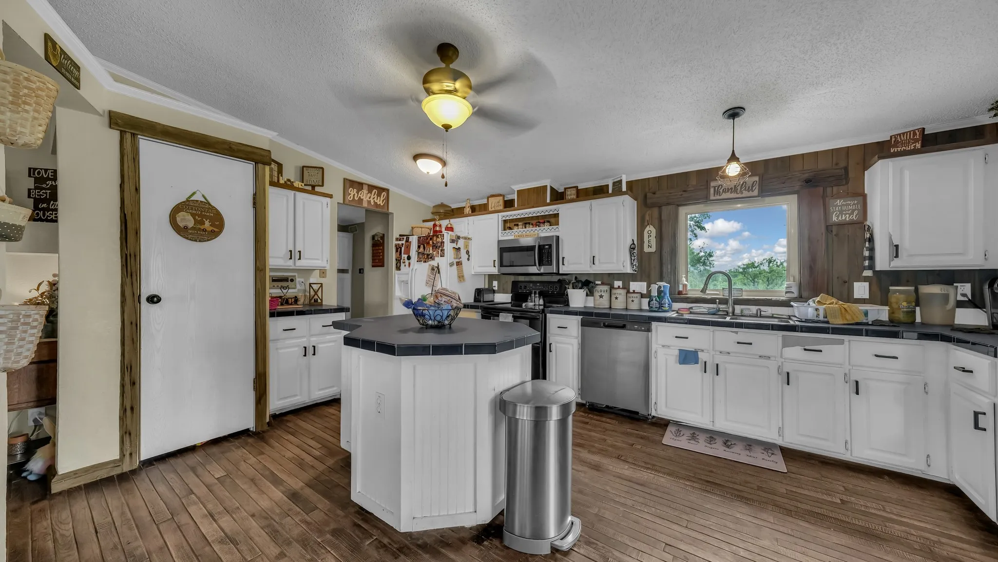 The kitchen features wood flooring, white cabinetry, and a central island with a dark countertop