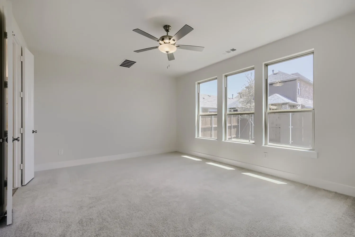 Spacious room featuring three large windows, light gray carpeting, and a ceiling fan with integrated lighting