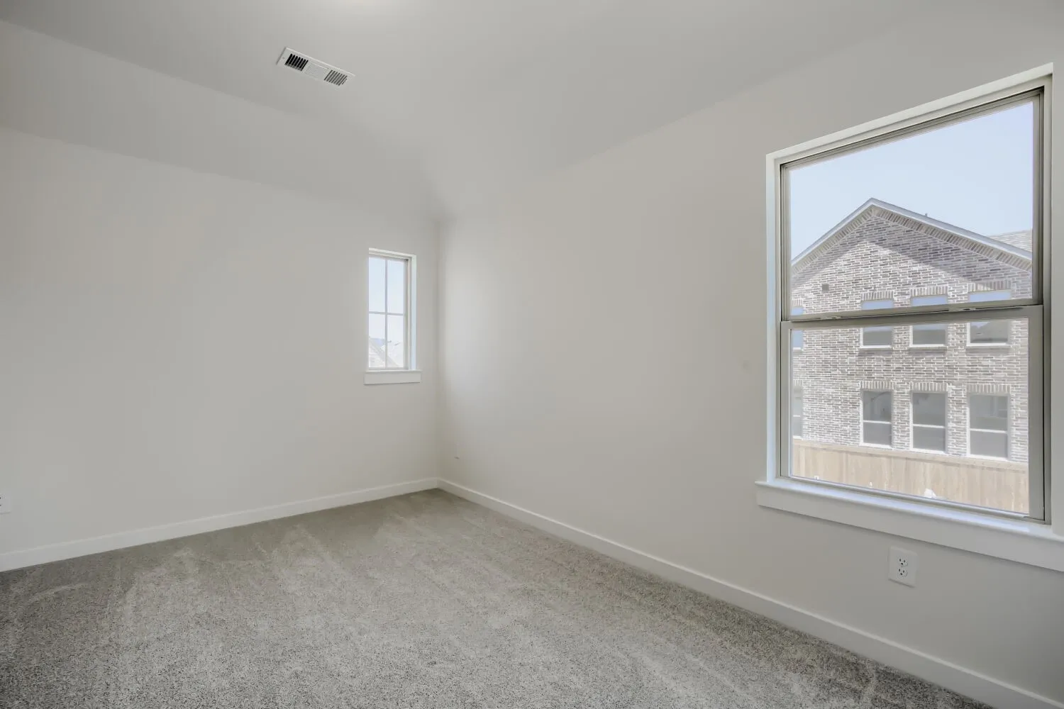 Light-filled room featuring neutral wall tones, gray carpeting, a large double-hung window, a smaller vertical window, and white trim throughout