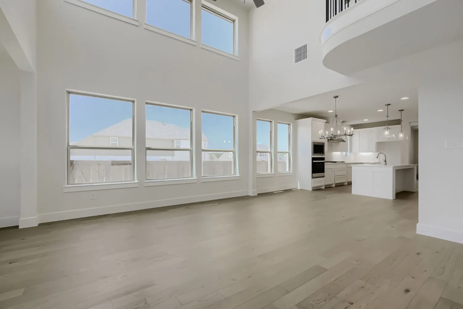 Open-concept living area featuring a two-story ceiling, light wood-finish flooring, and an abundance of natural light through multiple windows