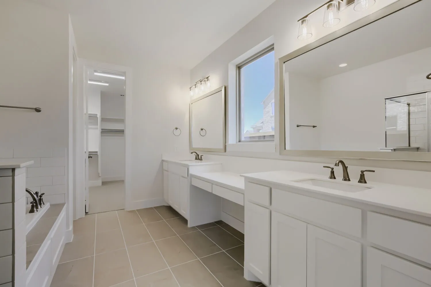 Bathroom featuring dual vanities with white cabinetry and countertops, framed mirrors, and bronze-finish fixtures