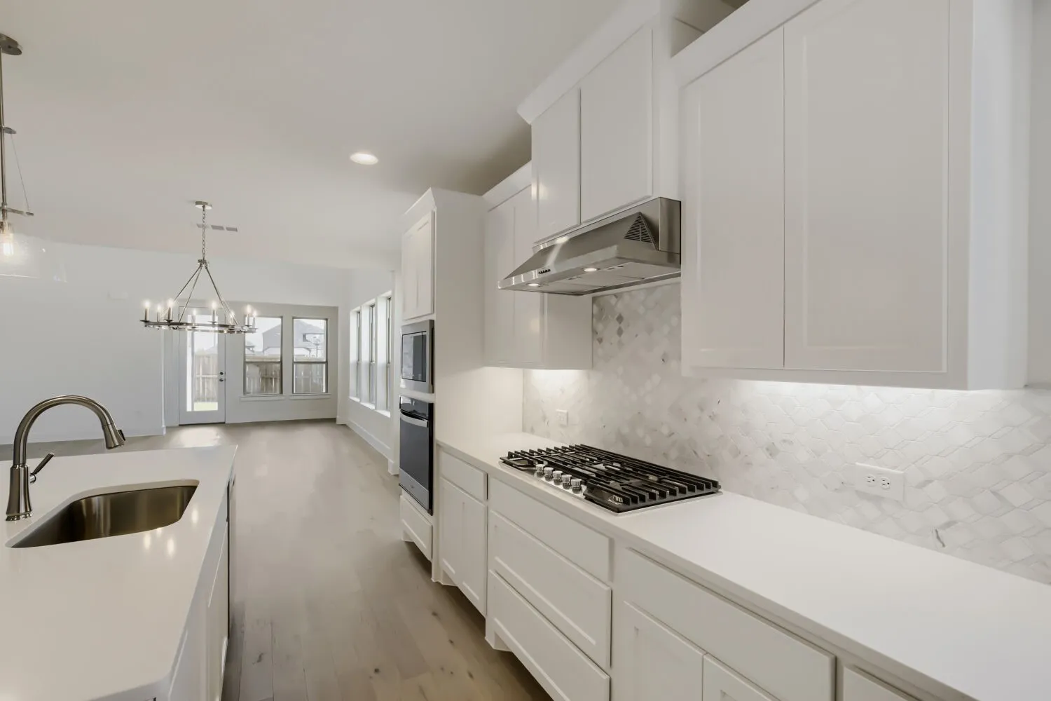 Kitchen featuring white shaker cabinetry, light-toned countertops, a stainless steel gas cooktop, built-in double ovens, and a patterned tile backsplash