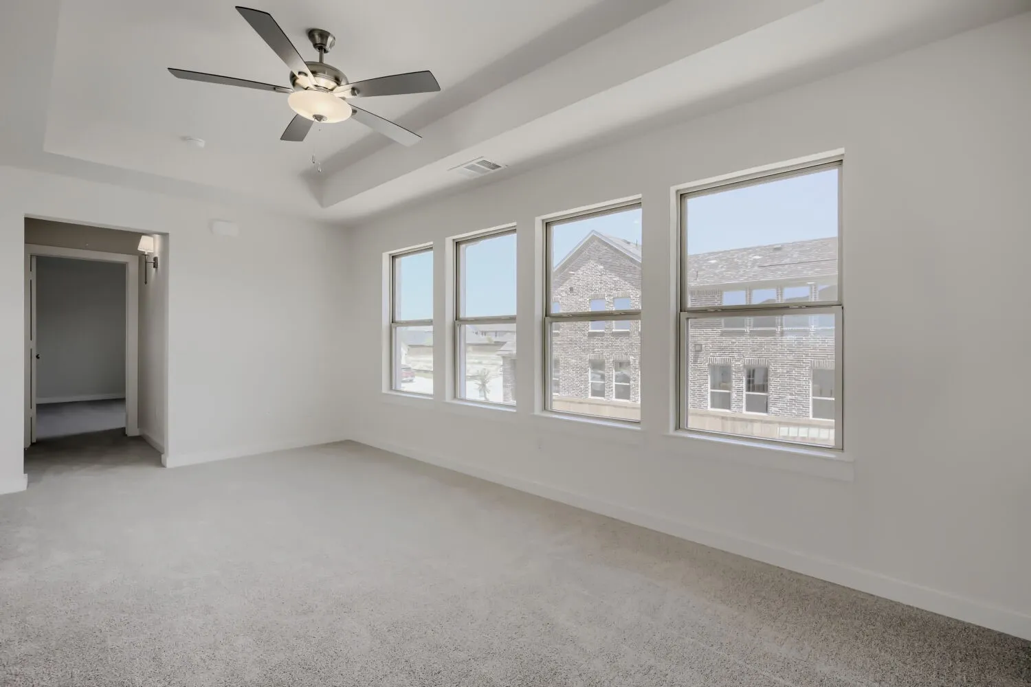 Spacious interior room featuring a tray ceiling, contemporary ceiling fan, light gray carpet, and a row of four windows