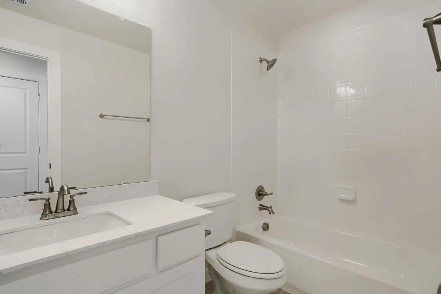 Bathroom featuring a white vanity with an integrated sink, a speckled light-toned countertop, a frameless wall mirror, and a white bathtub with a tiled surround