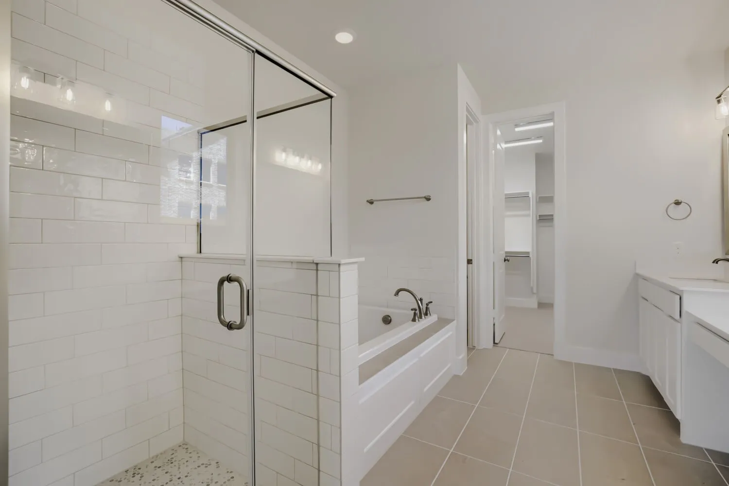 Spacious bathroom featuring a glass-enclosed shower with white subway tile, a built-in soaking tub, and neutral-toned floor tiling